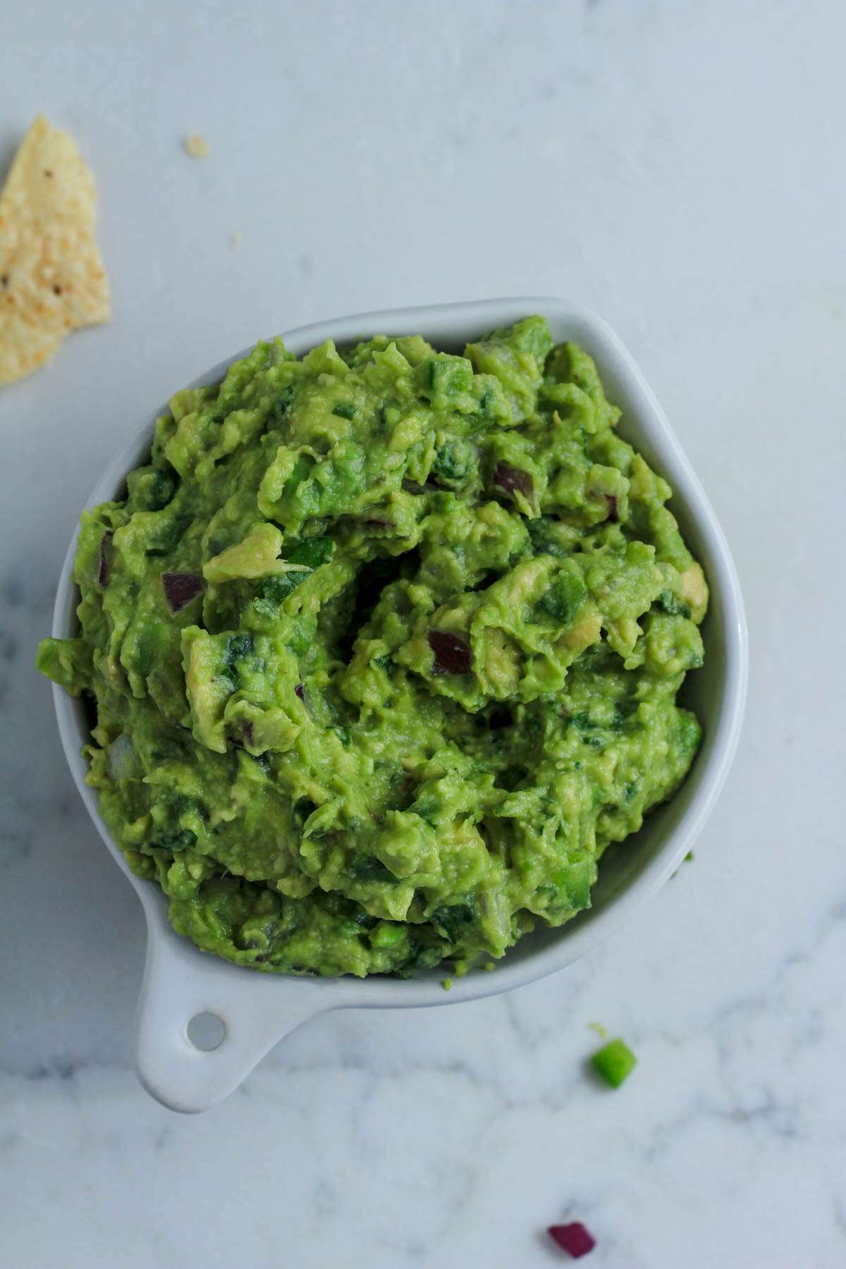 A small white bowl topped with guacamole on a white counter.