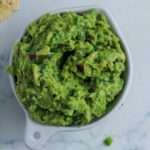 A close up of a small white bowl filled with vegan guacamole on a white counter.