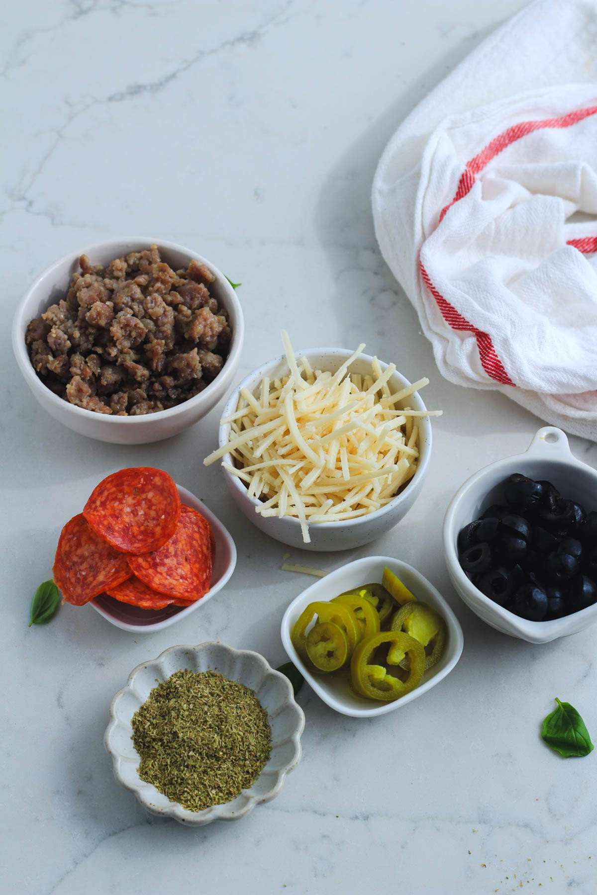 Different dairy-free toppings for pizza quesadillas in bowls on a white counter.