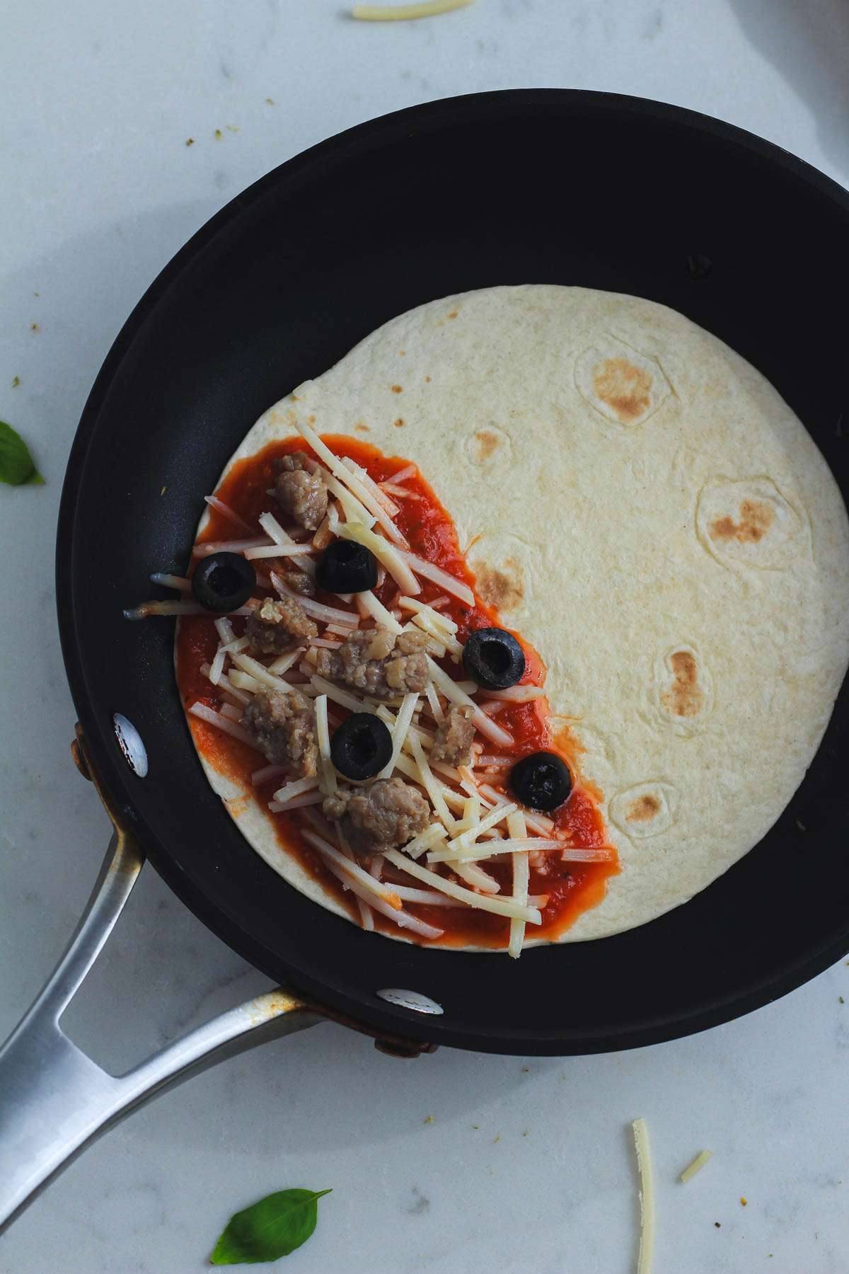 A dairy-free pizzadilla topped with sausage and olives before cooking.