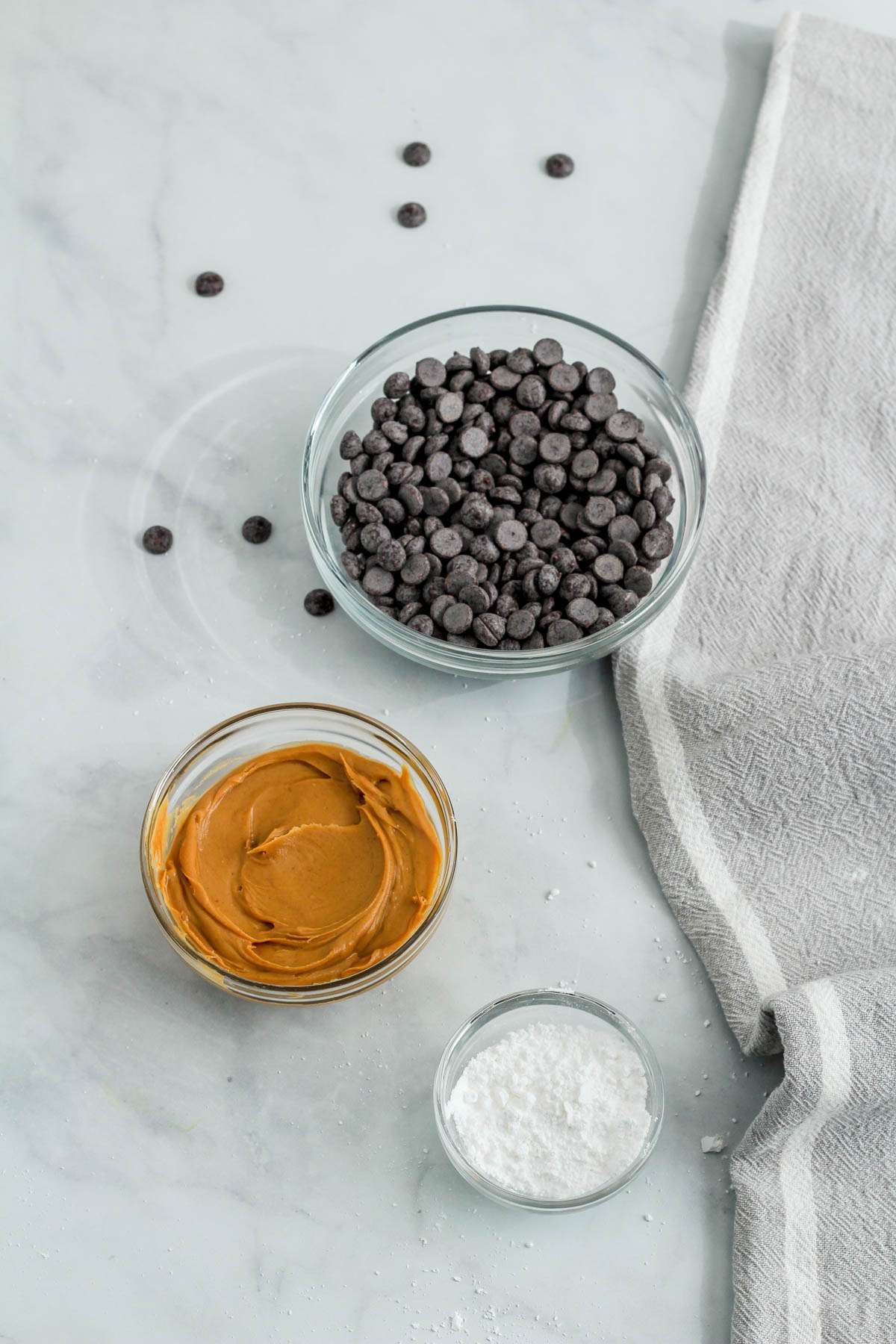 Ingredients for vegan peanut butter cups on a white ish counter with some chocolate chips scattered about.