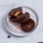 Four vegan peanut butter cups on a white plate with one missing a bite.
