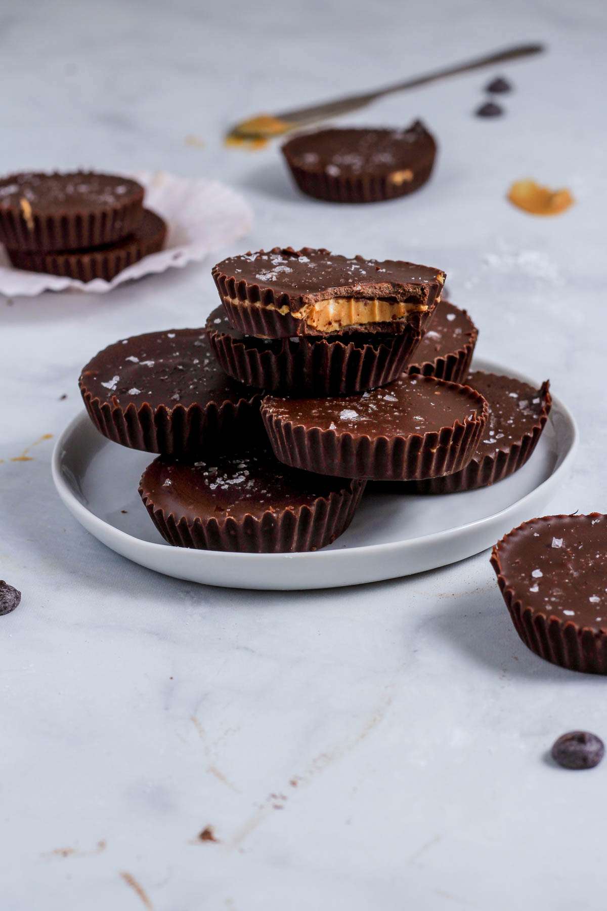 A stack of vegan peanut butter cups on a white plate with the top cup missing a bite.