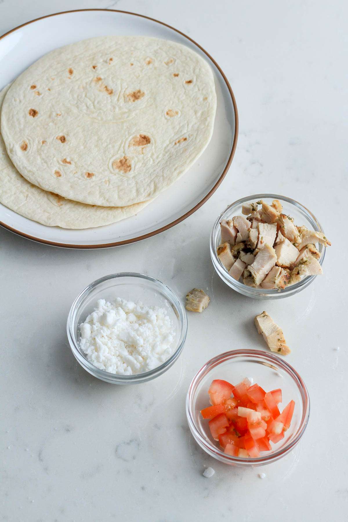 A white counter with the base ingredients for a Greek Chicken Quesadilla.