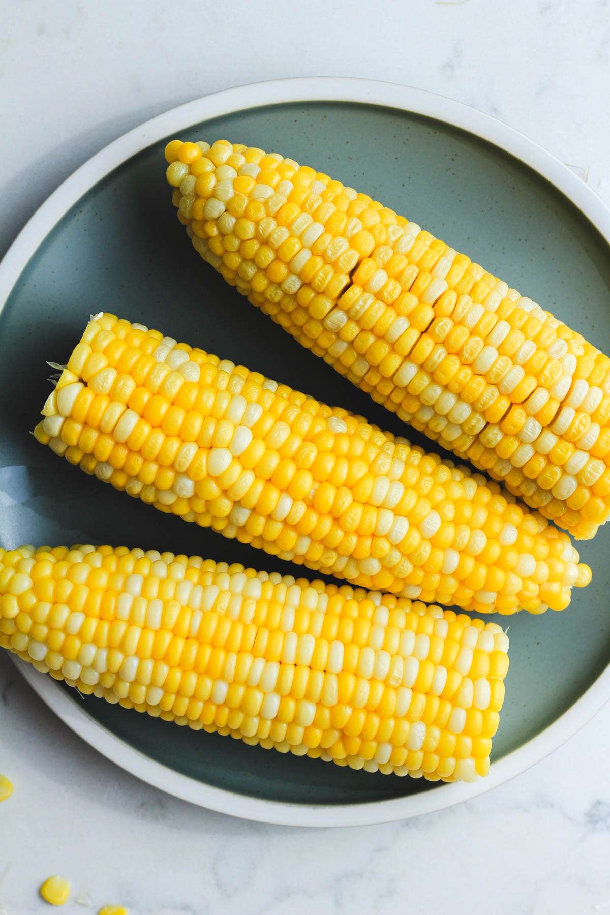 A green plate topped with three ears of corn after cooking in the microwave.