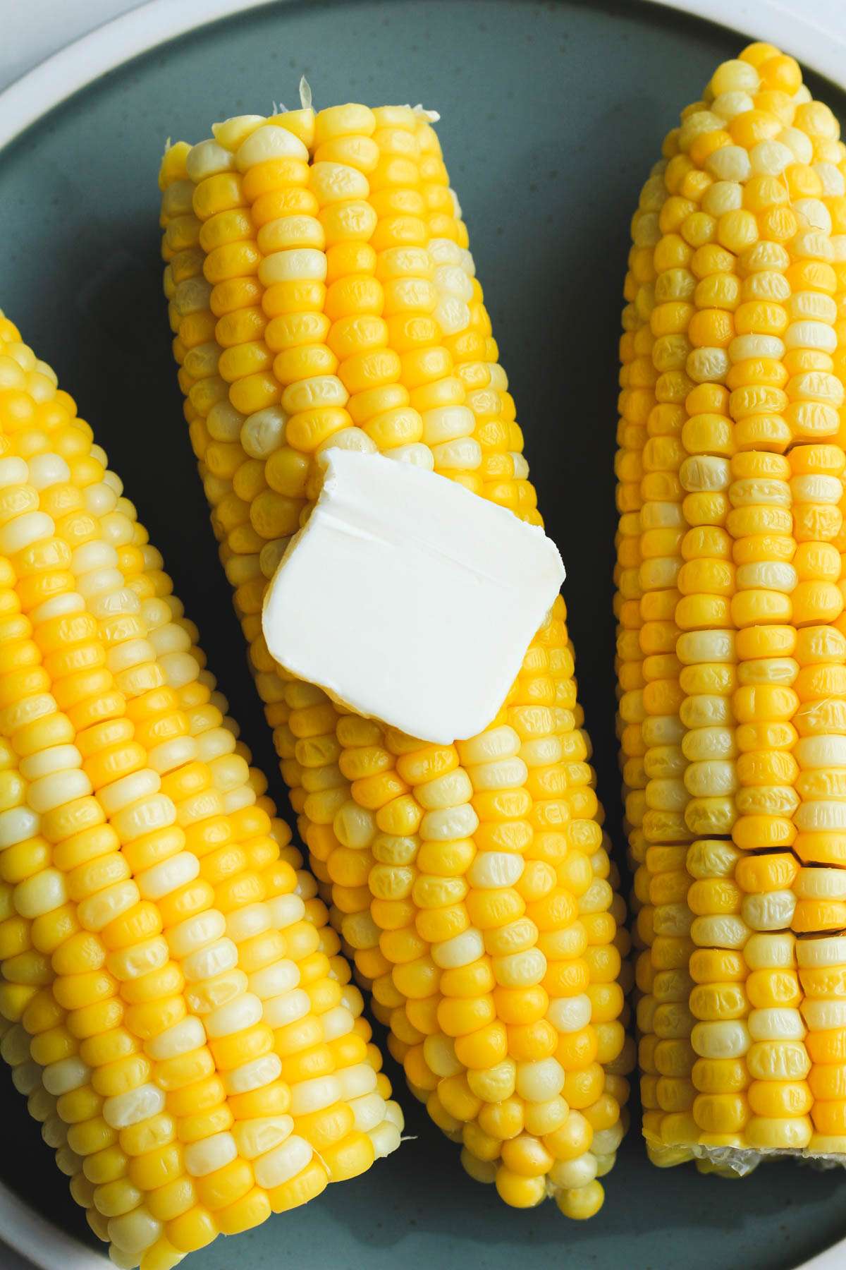 A small pat of vegan butter on an ear of microwave corn on a green plate.