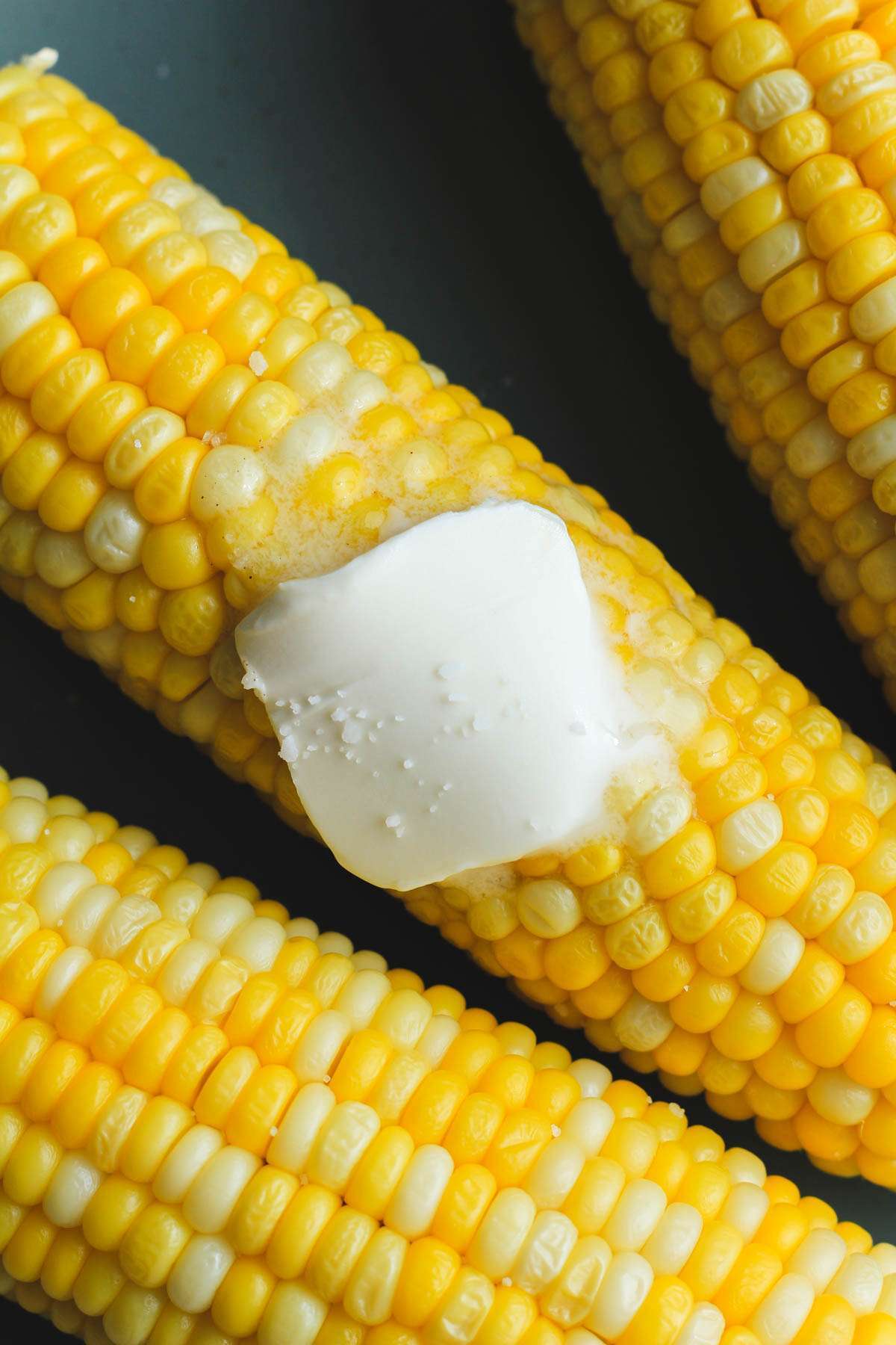 Melted vegan butter and salt on microwave cooked corn on a green plate.