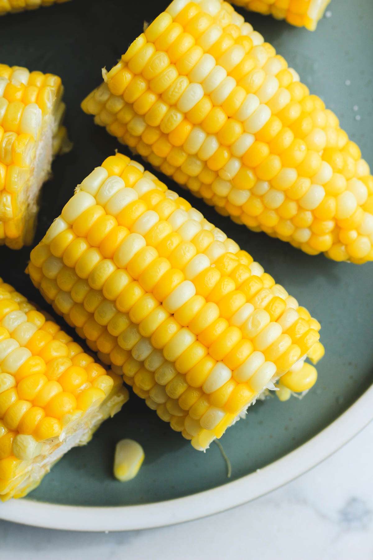 A green plate topped with cut pieces of microwave corn on the cob.