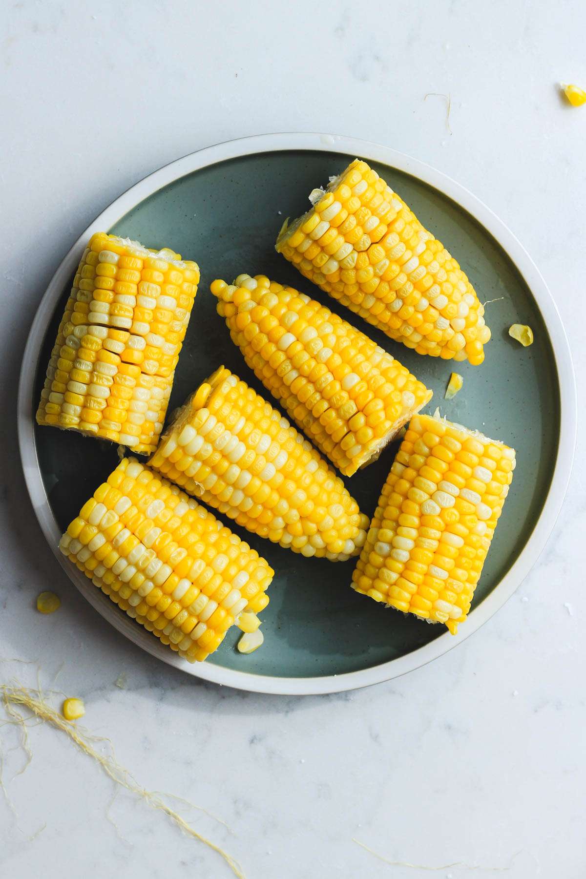 A green plate filled with pieces of corn to teach how to microwave corn on the cob.