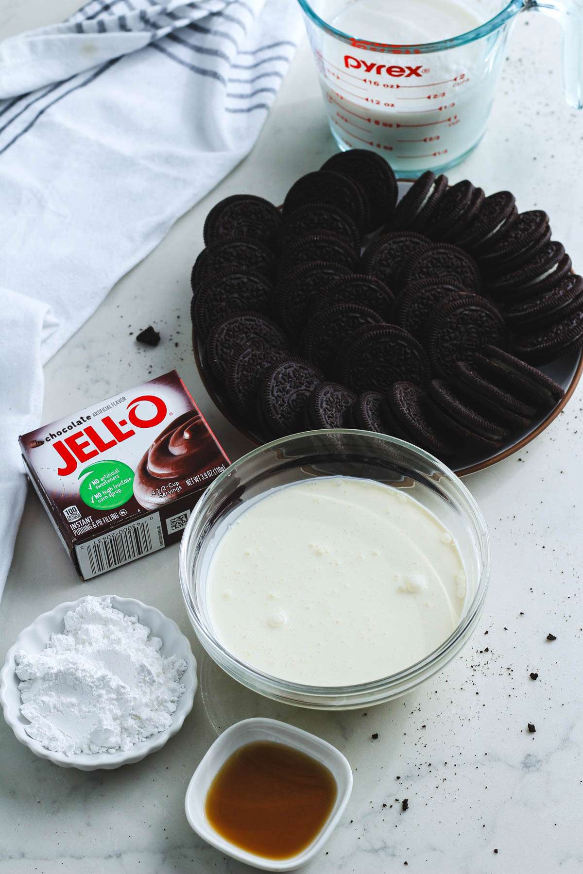 Ingredients for the Oreo Ice Box cake on a white counter with a white and blue dish towel to the left.