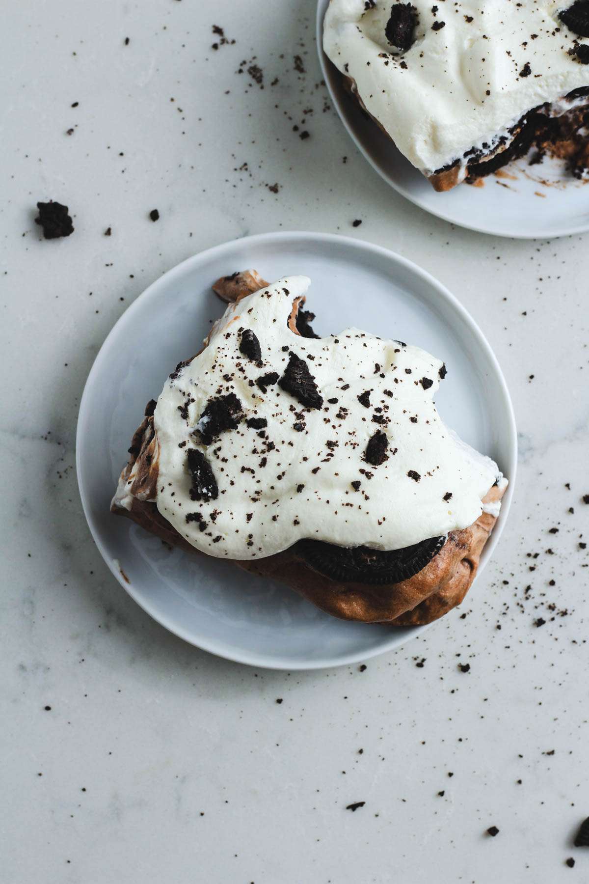 No bake Oreo ice box cake scooped on a white plate with some Oreo crumbs on the counter.