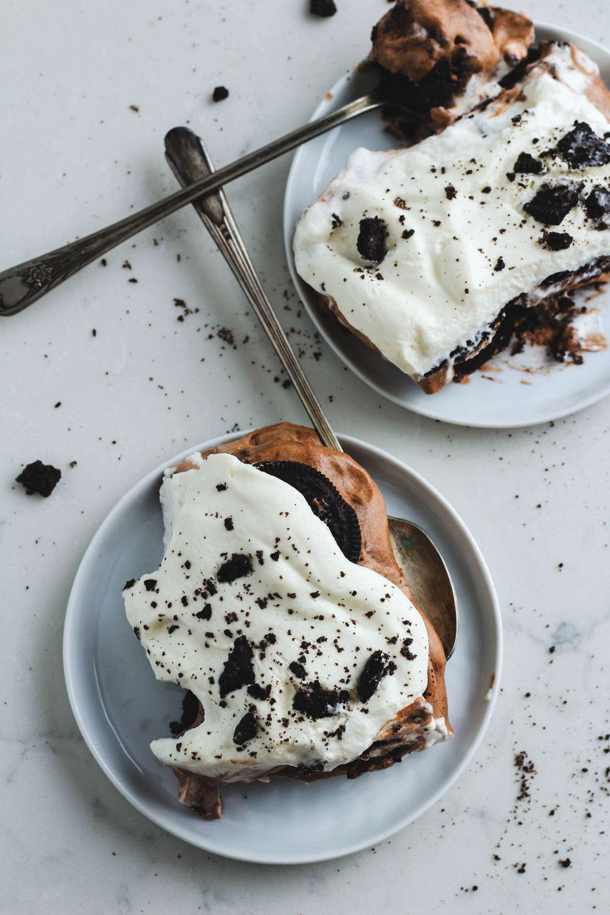 Two small white plates with scoops of no bake Oreo ice box cake and a silver spoon on each plate.