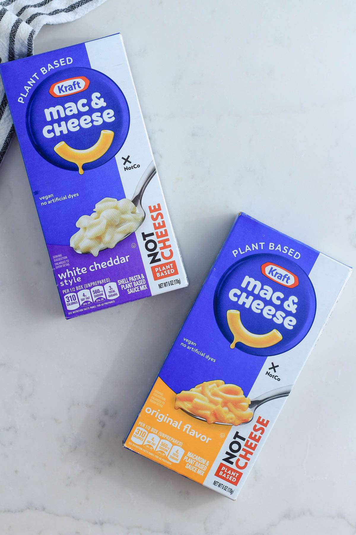 A box of white cheddar style and original flavor plant-based Kraft mac and cheese on a white counter.