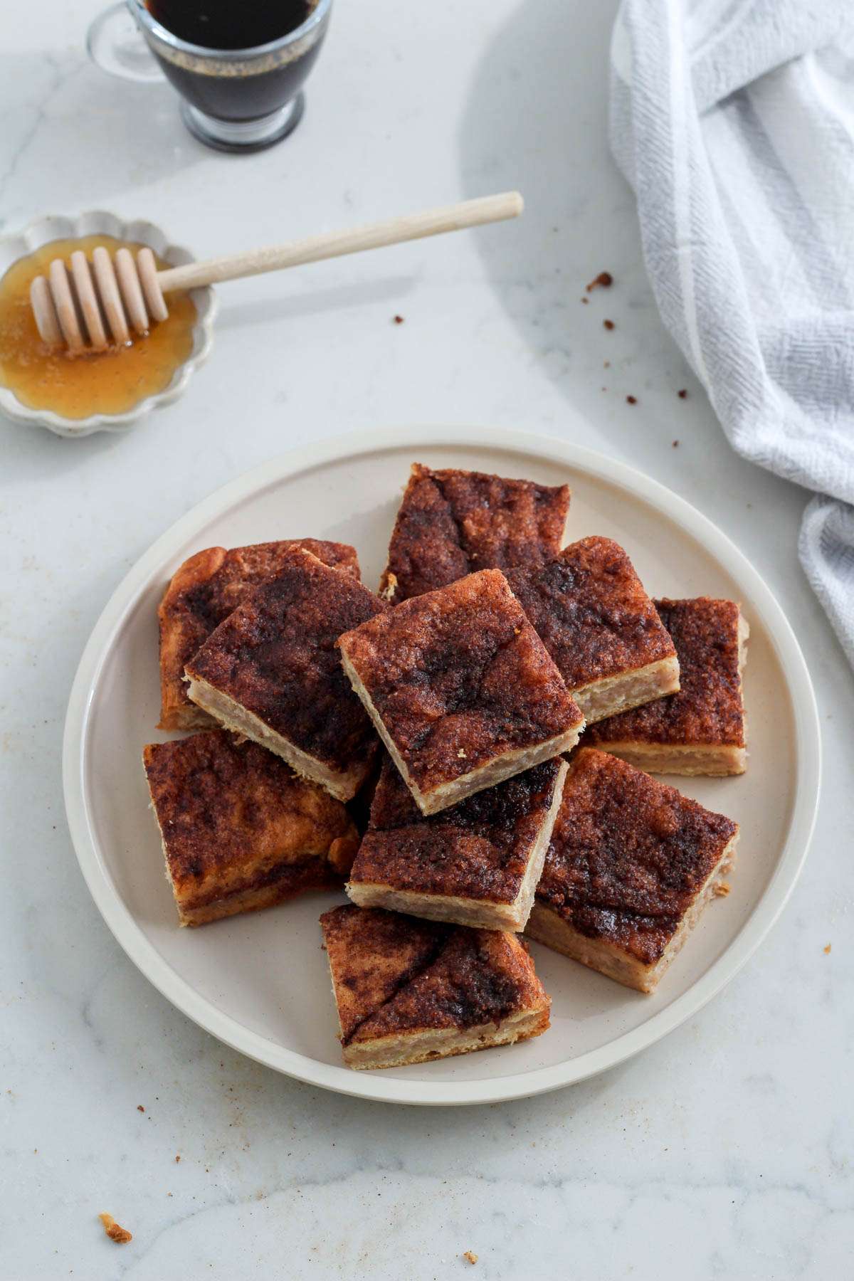 A small white plate with three layers of sopapilla cheesecake bars with a small bowl of honey in the back left corner.