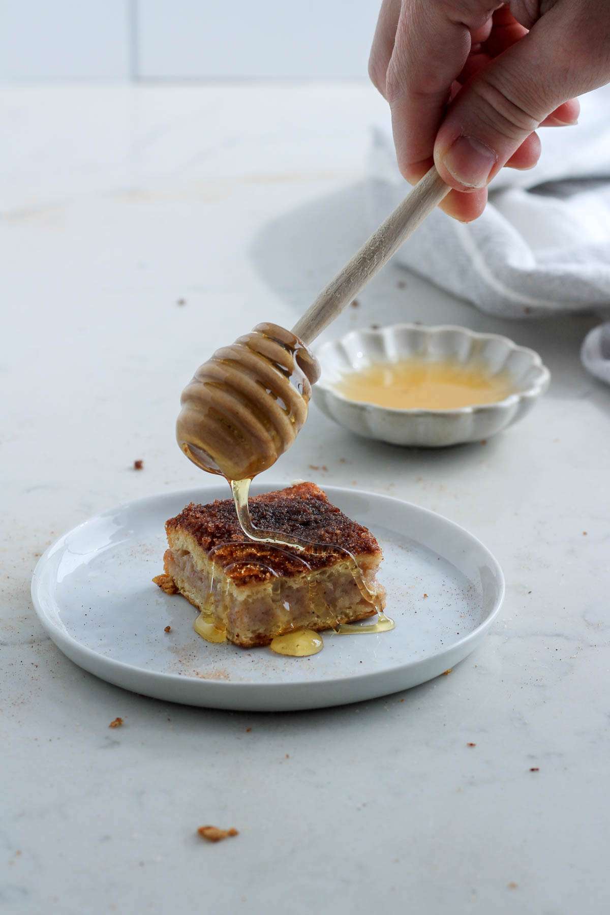 A small white plate with a sopapilla cheesecake bar being drizzled with honey over the top.
