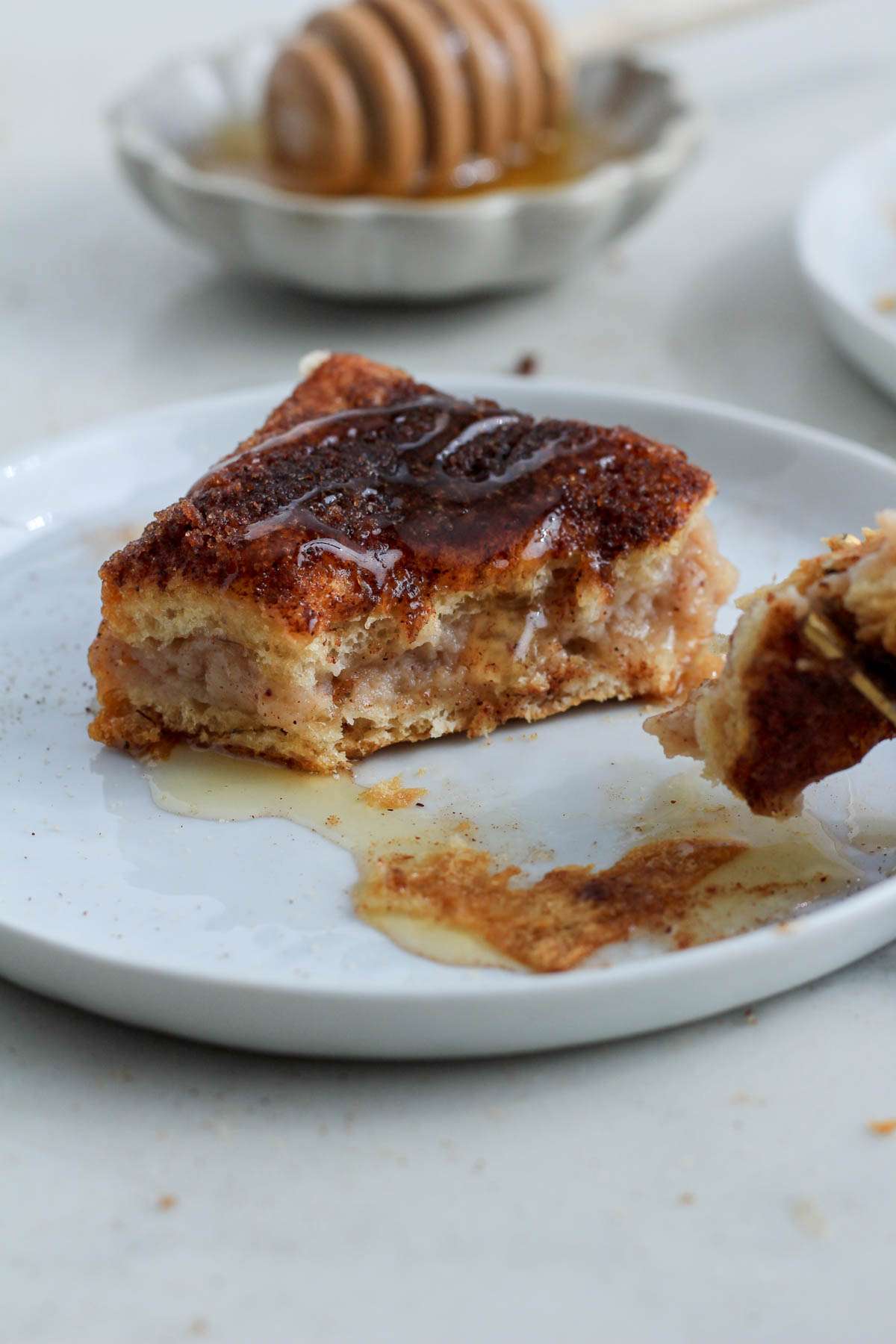 A honey drizzled sopapilla cheesecake bar on a white plate with a bite pulled to the front.