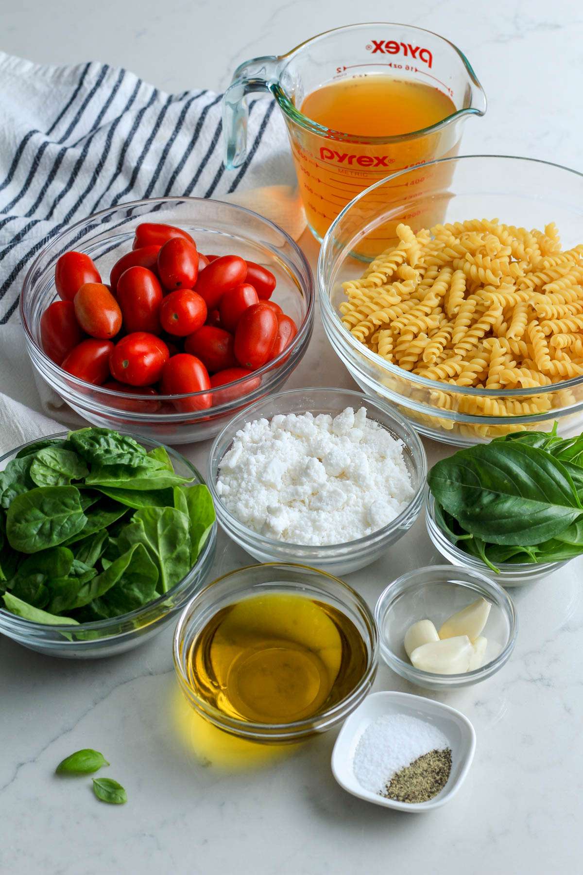 Ingredients for vegan baked feta pasta on a white counter with a blue and white striped towel.