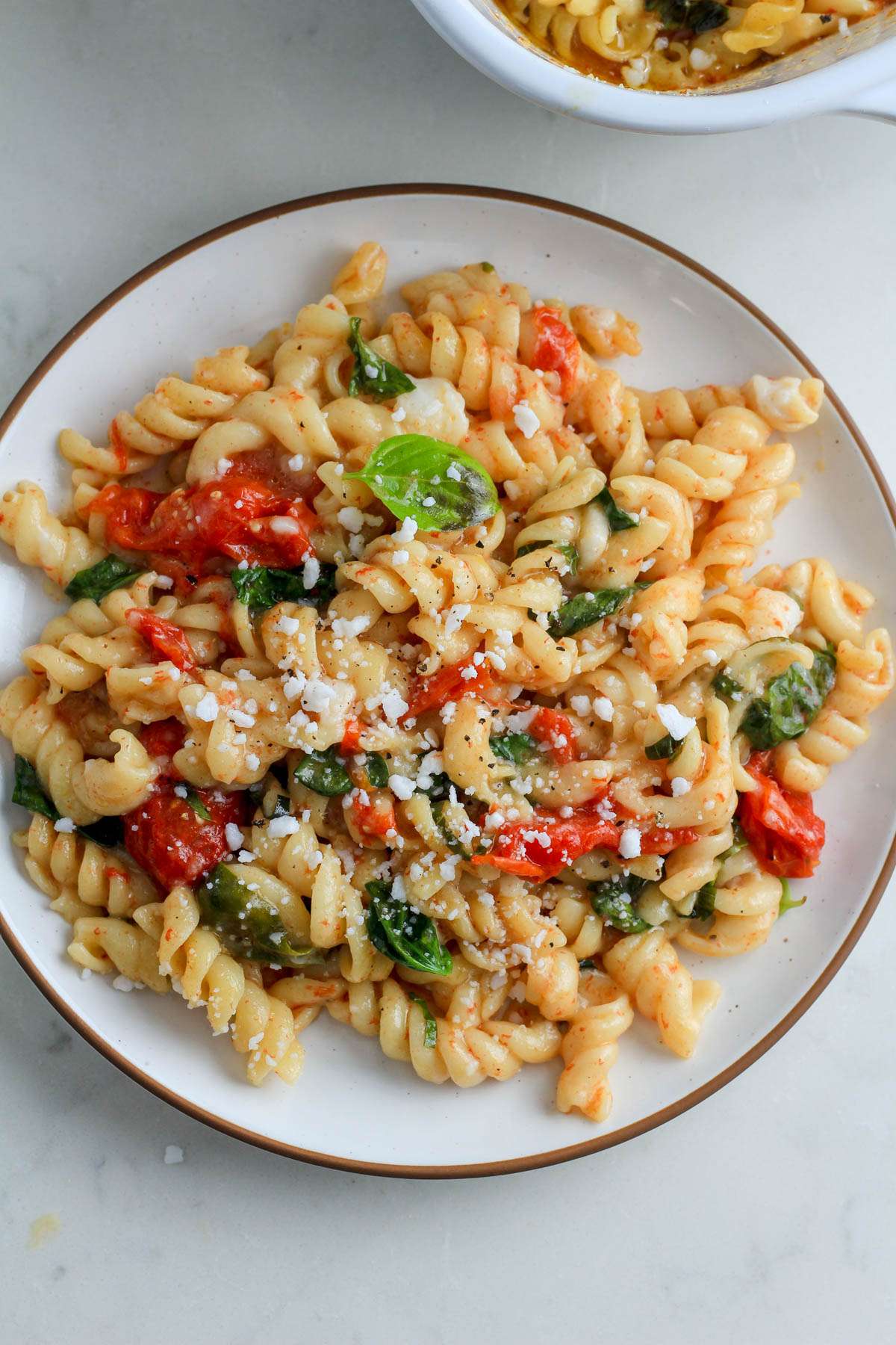 A top down image of vegan baked pasta with feta on a white plate with a brown rim.
