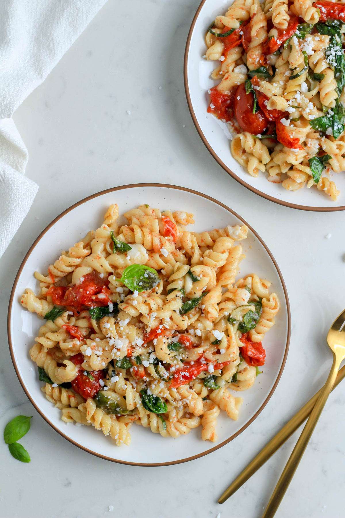 Two white plates with brown rims topped with baked feta pasta on a white counter.