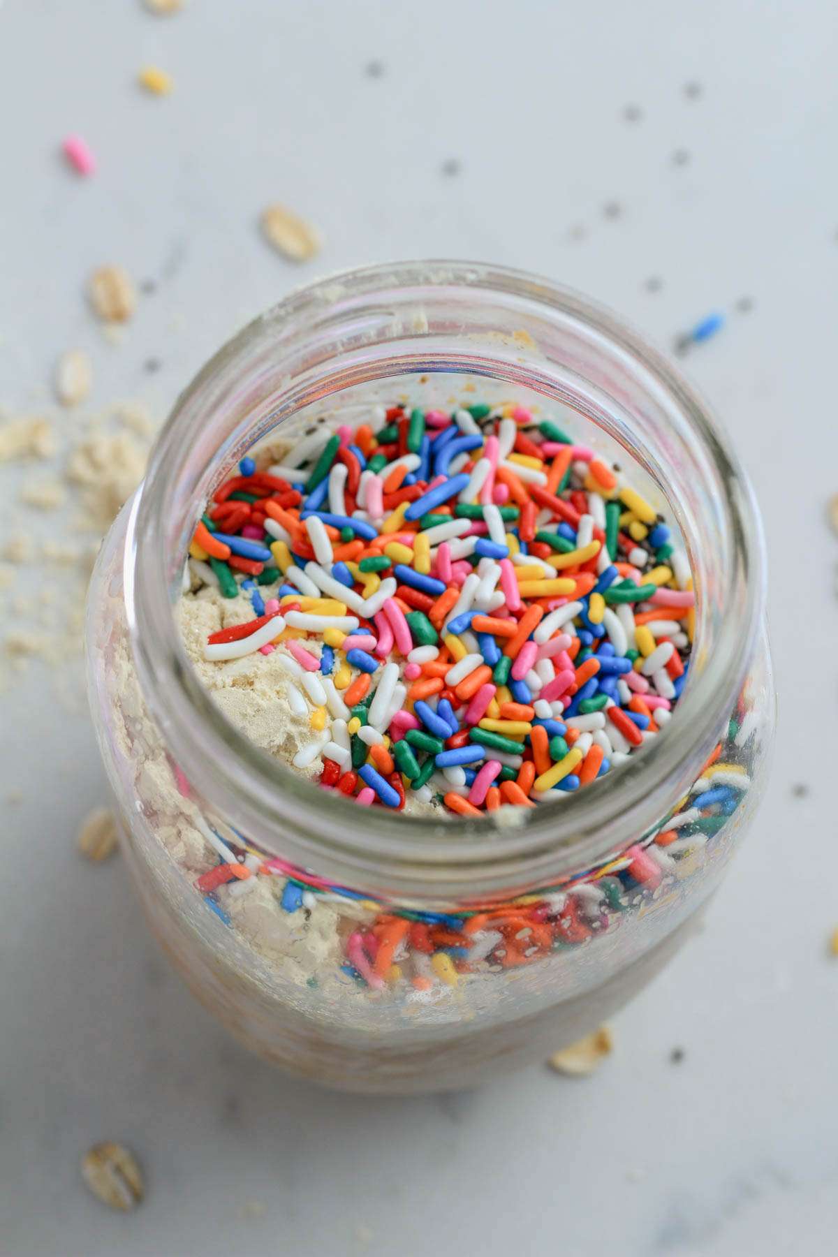 A top down photo of a glass mason jar with vegan birthday cake overnight oats before mixing on a white counter.