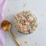 A small white bowl filled with vegan birthday cake overnight oats topped with colorful sprinkles.