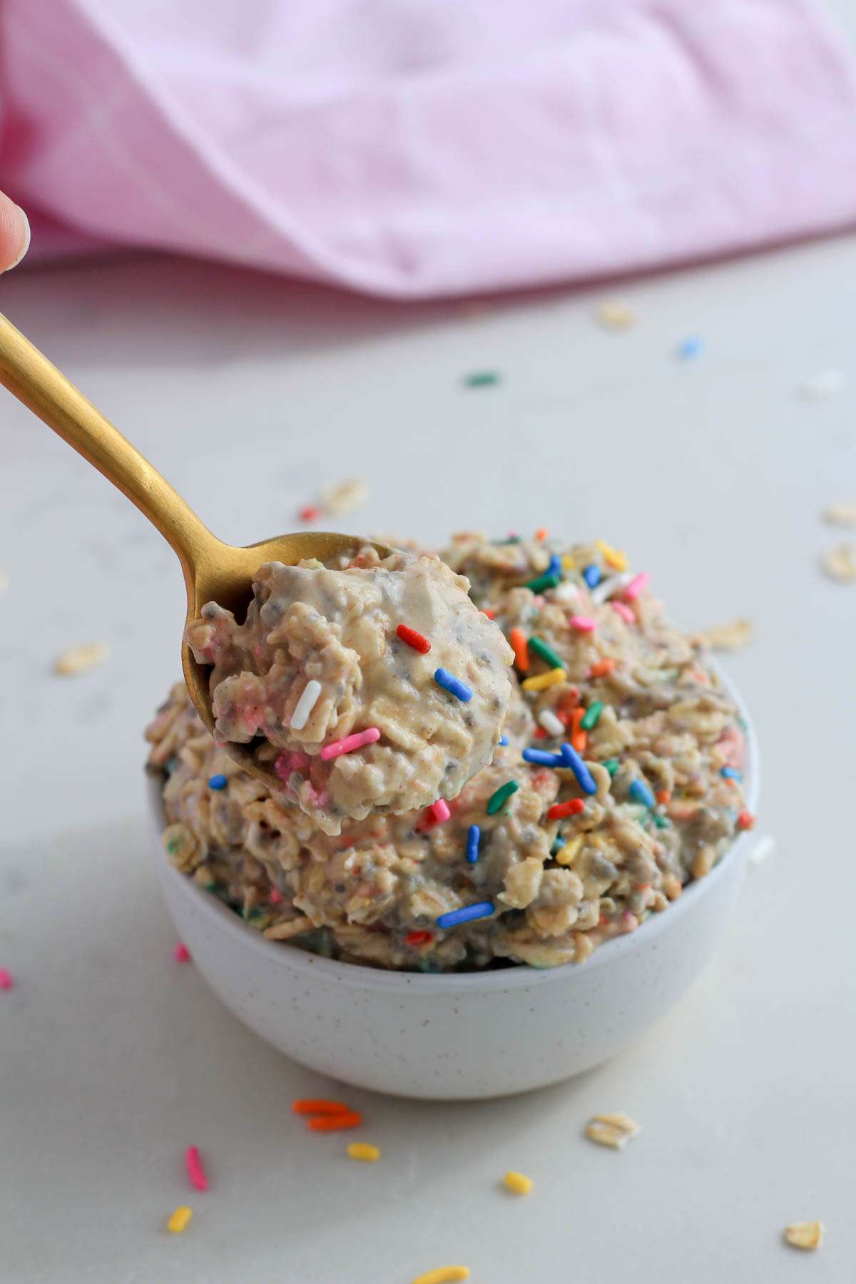 A gold spoon with a small scoop of vegan overnight oats in front of a white bowl.