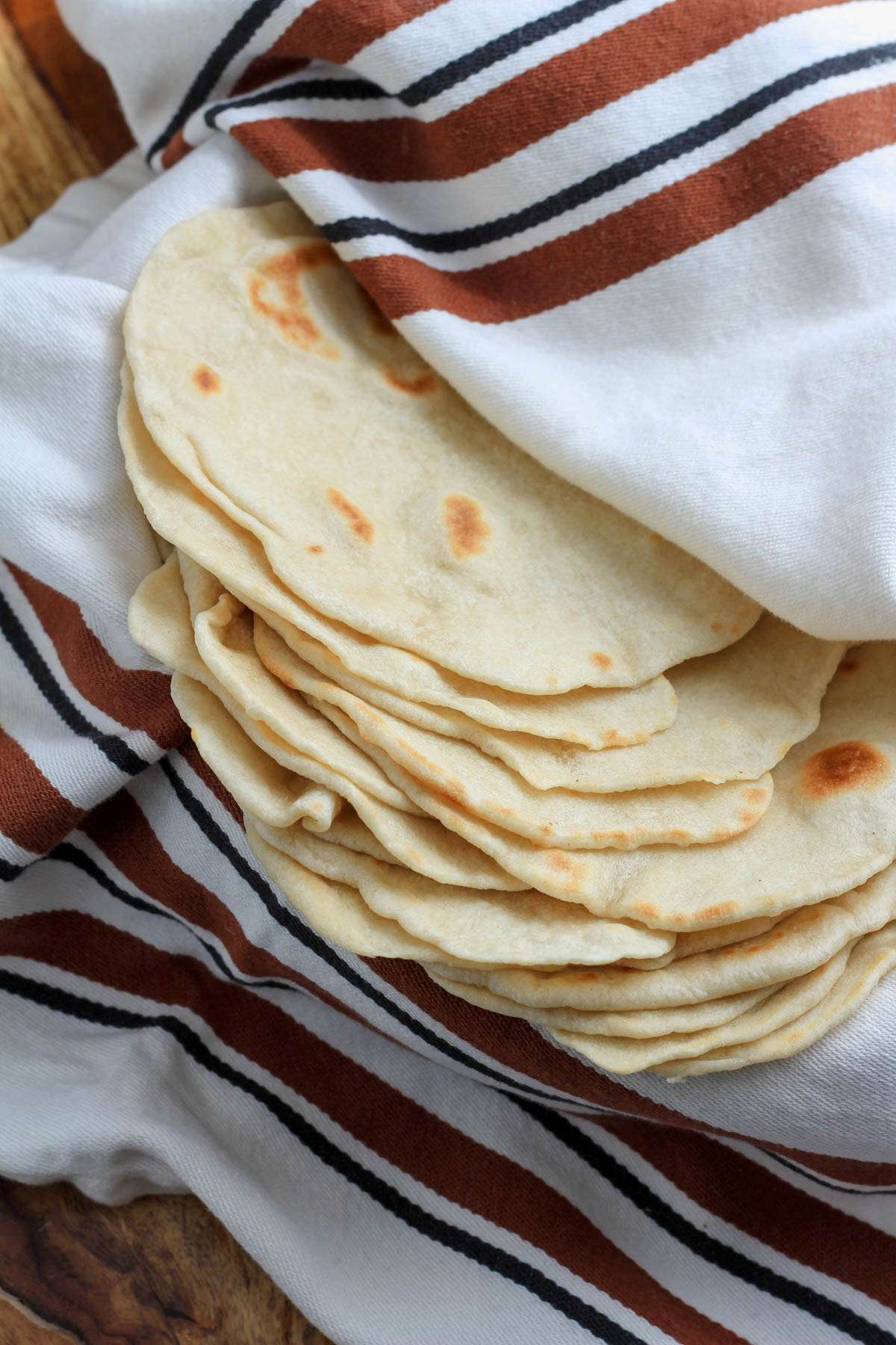 A white towel with brown and black lines filled with a stack of vegan flour tortillas.