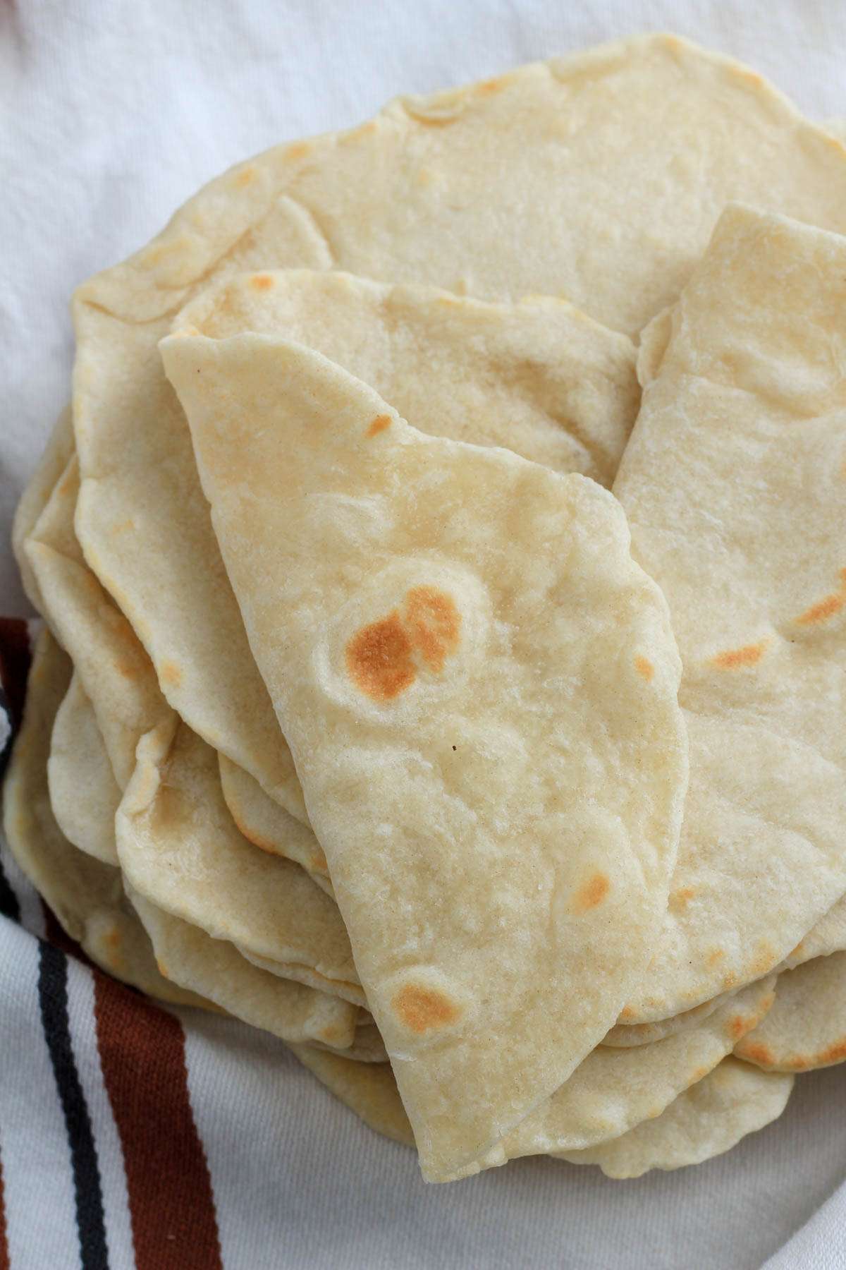 A white dish towel topped with flour tortillas bent to show flexibility.