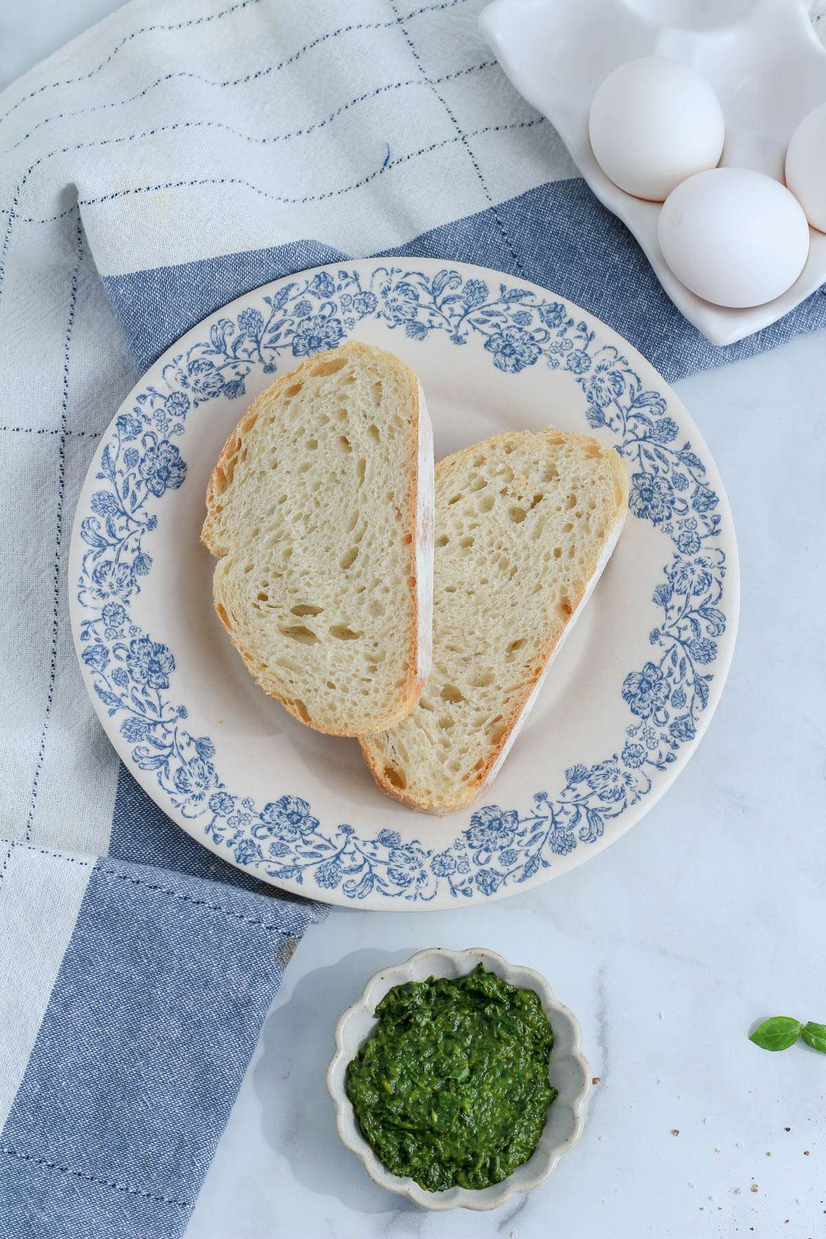 A white and blue plate with sliced bread and a small dish with spinach pesto in front.