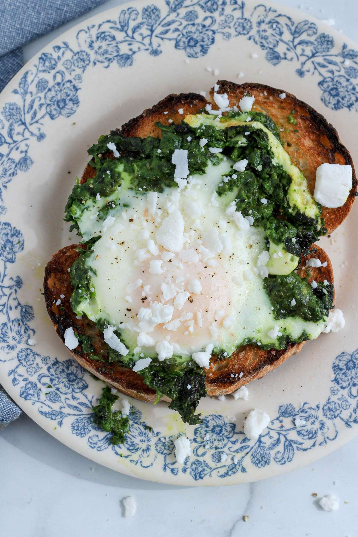 A top down picture of a white and blue plate with a slice of pesto egg toast topped with dairy-free feta cheese.