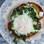 Pesto fried egg toast topped with dairy-free feta on a white and blue plate.