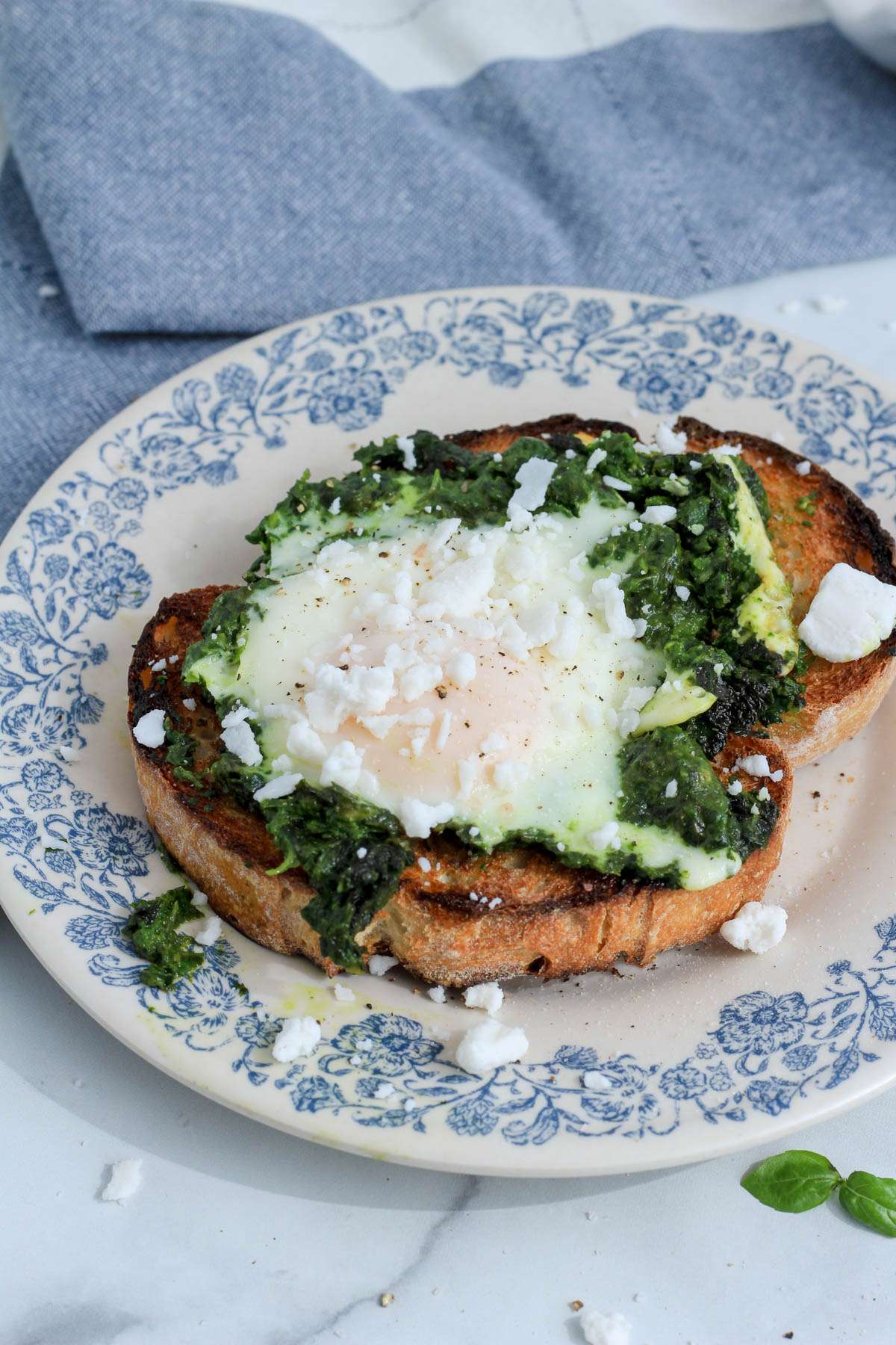 Dairy-free pesto egg on toast on a white and blue plate with a blue and white towel in the back left.