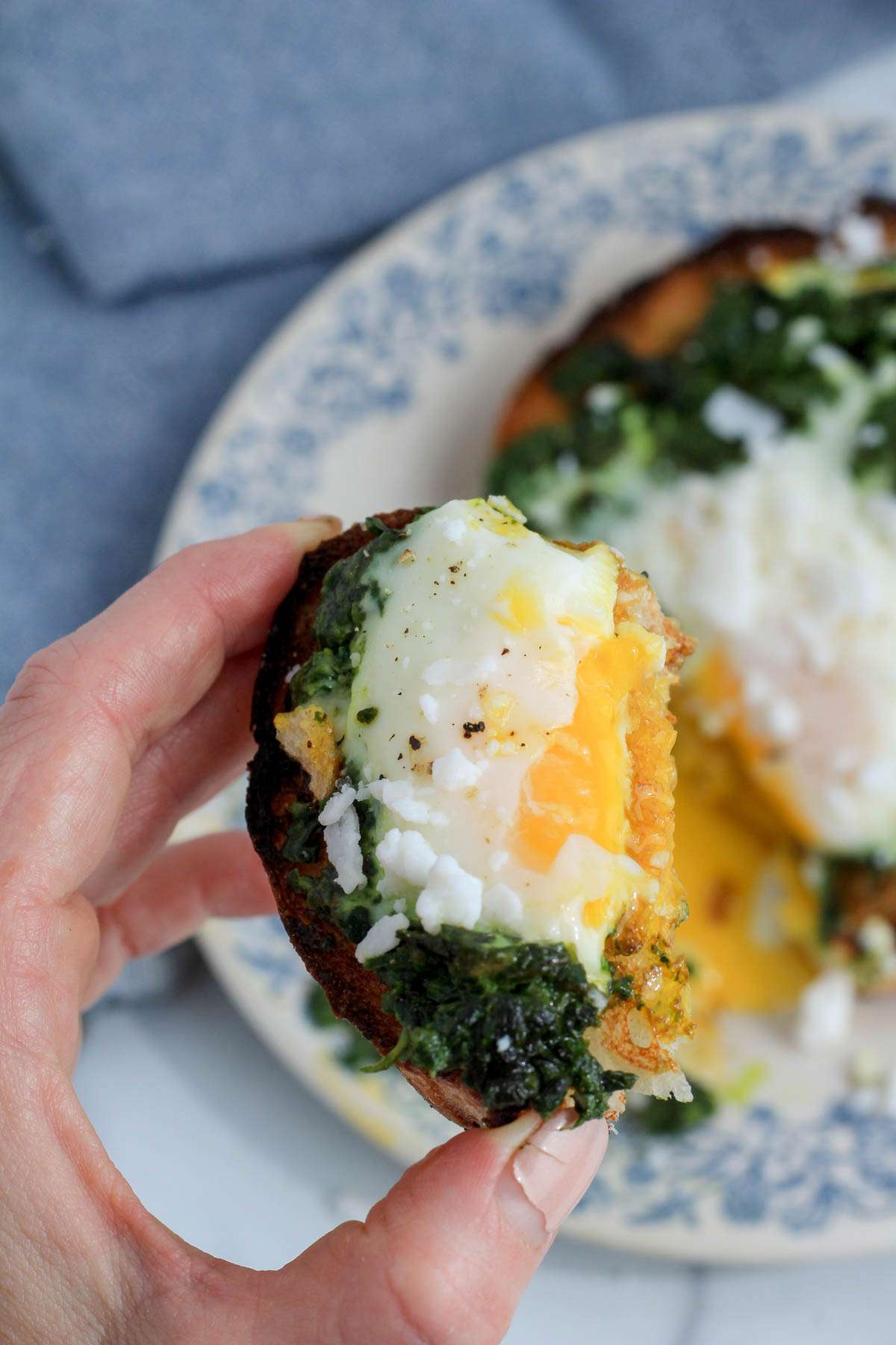 A hand holding a slice of pesto egg toast with bright yellow egg yolk.