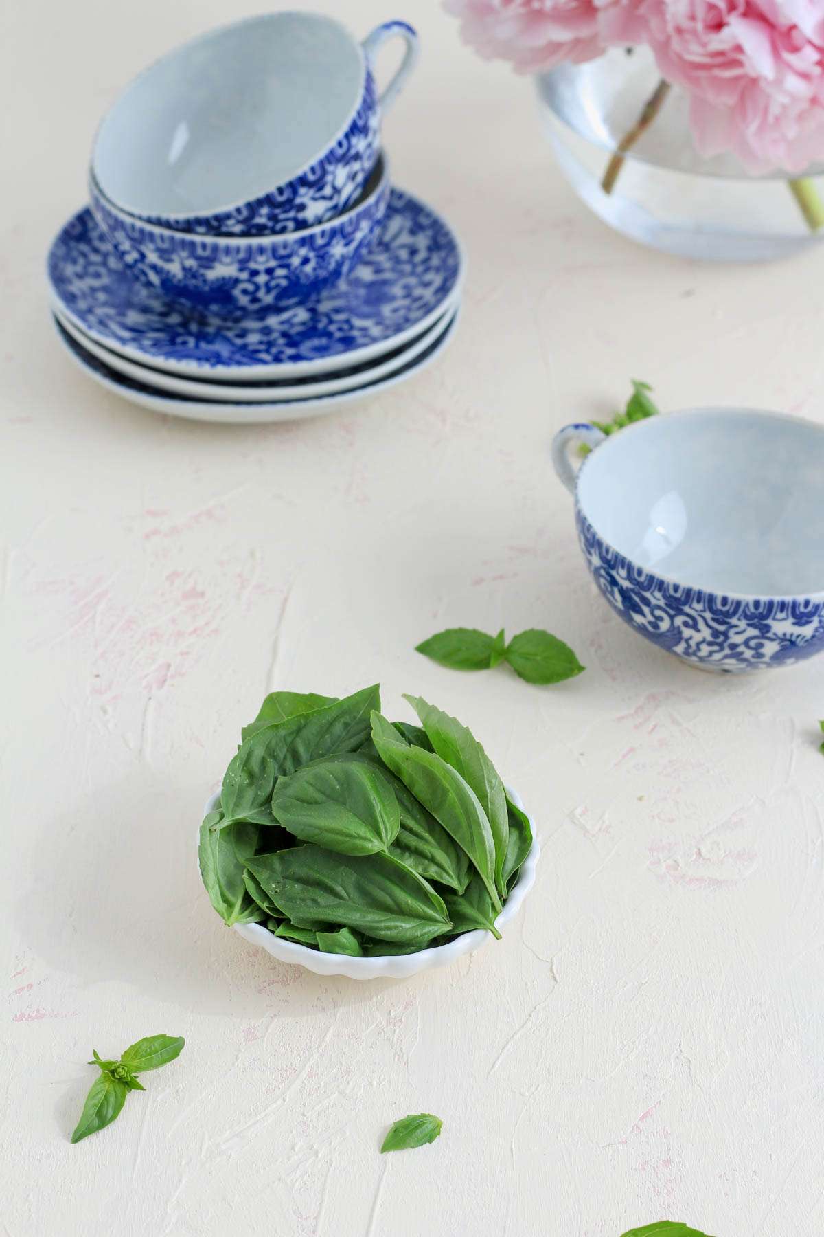 Ingredients for fresh basil tea on a white counter with blue and white cups in the back.