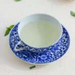 A white and blue tea cup filled with fresh basil tea on a white counter.