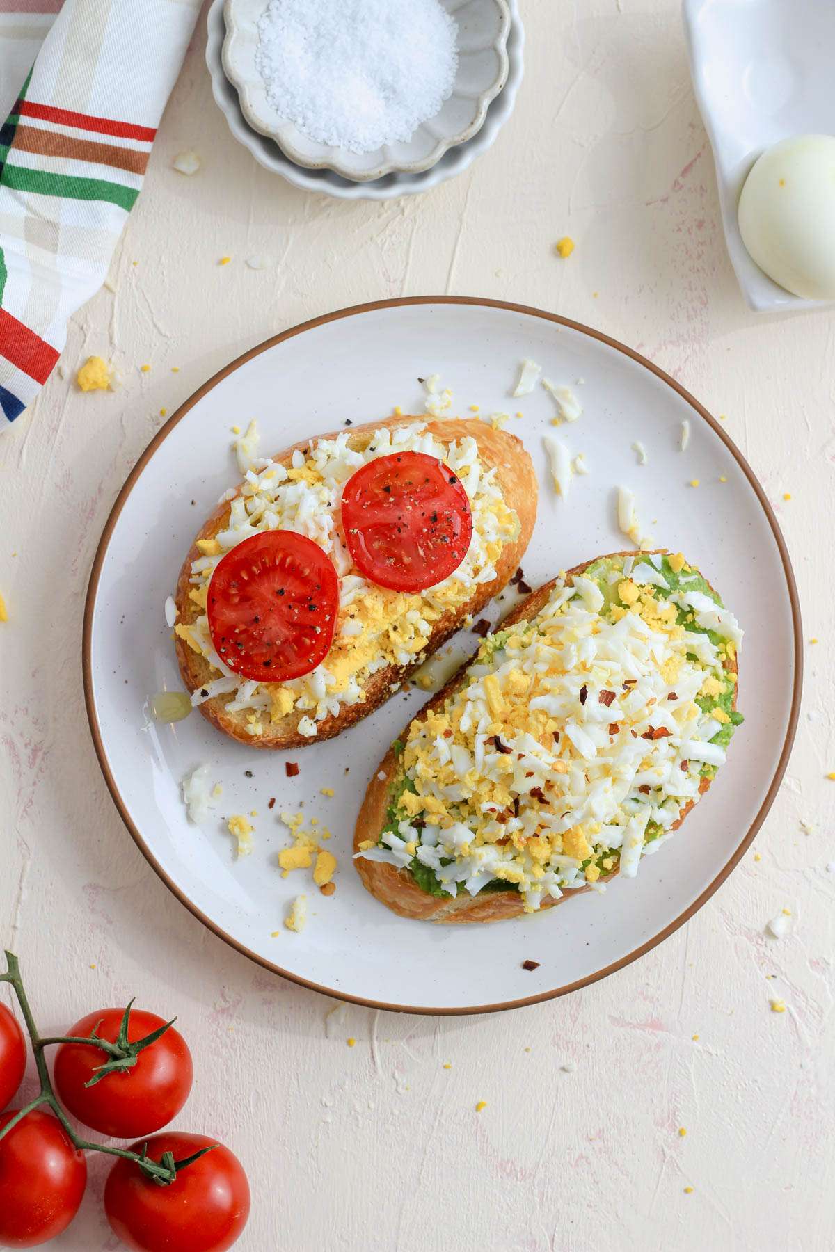 A top down picture of two slices of grated egg on toast one on the left with two slices of tomato and the one on the right with avocado.