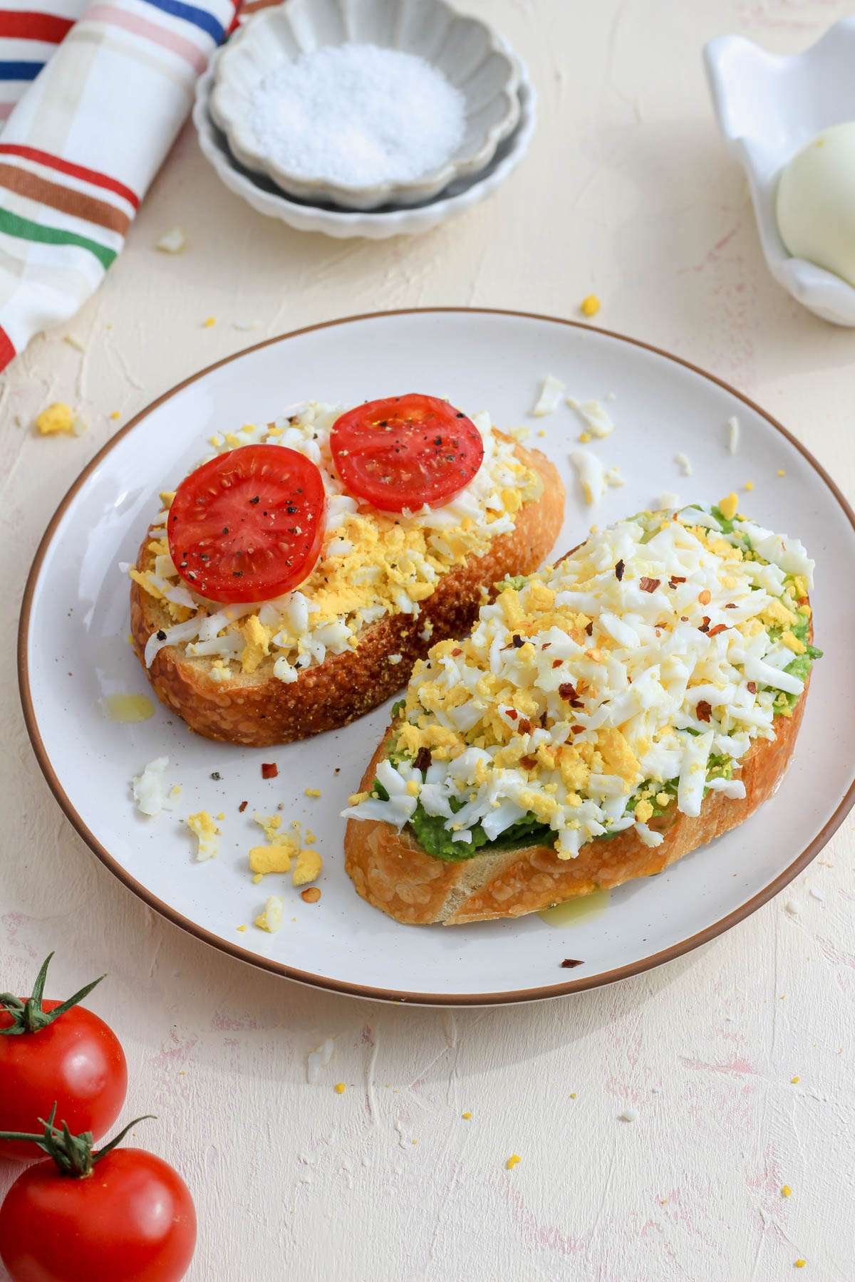 A white plate with grated hard boiled egg toast on a cream counter with a plate of salt in the back left.
