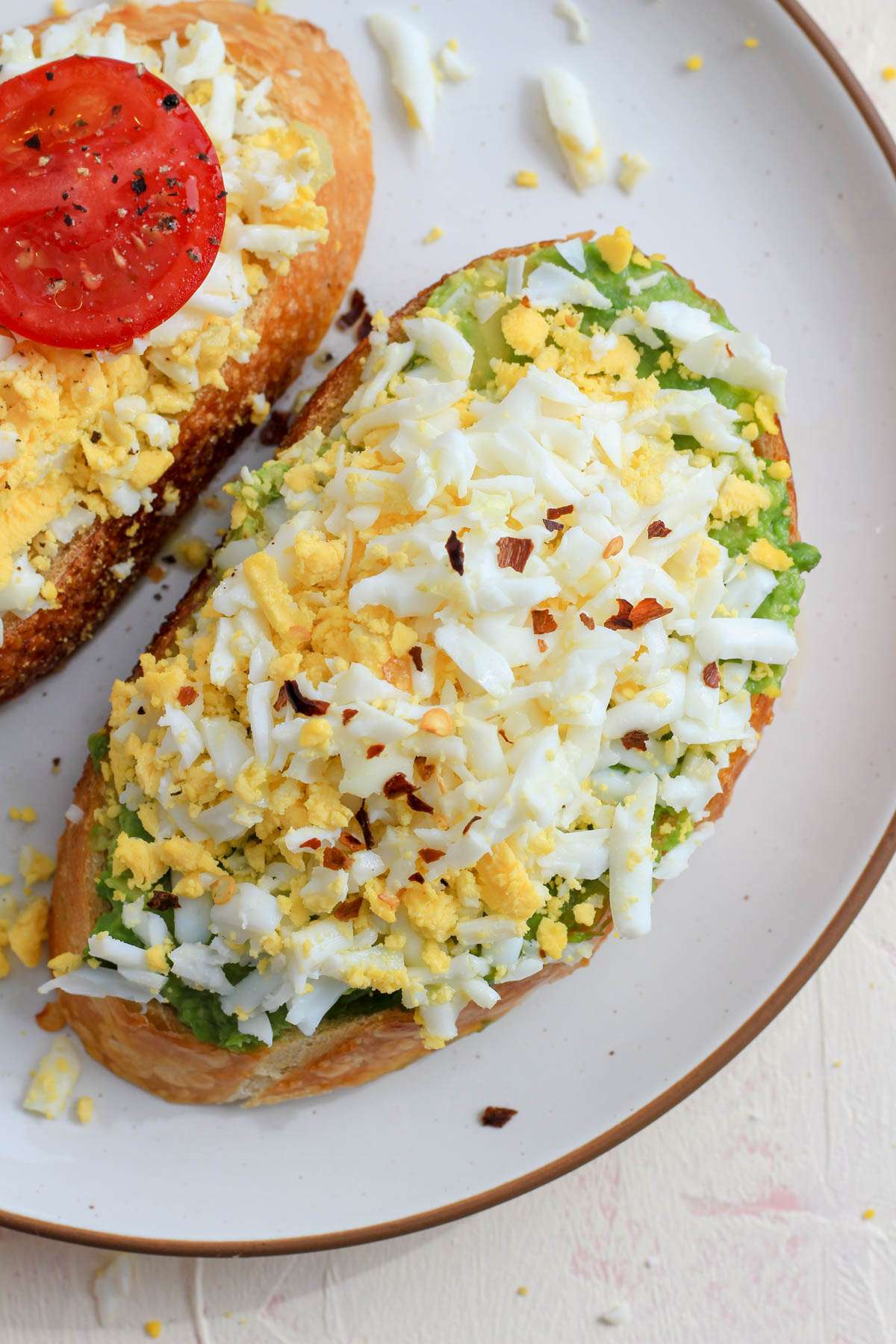 A top down picture of a slice of avocado toast topped with a grated hard boiled egg and red pepper flakes.