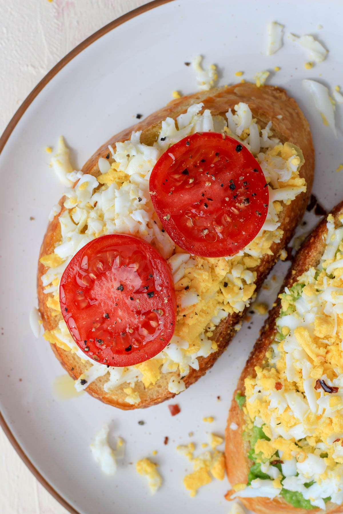 A white plate with a slice of grated hard boiled egg on toast with two slices of tomato.