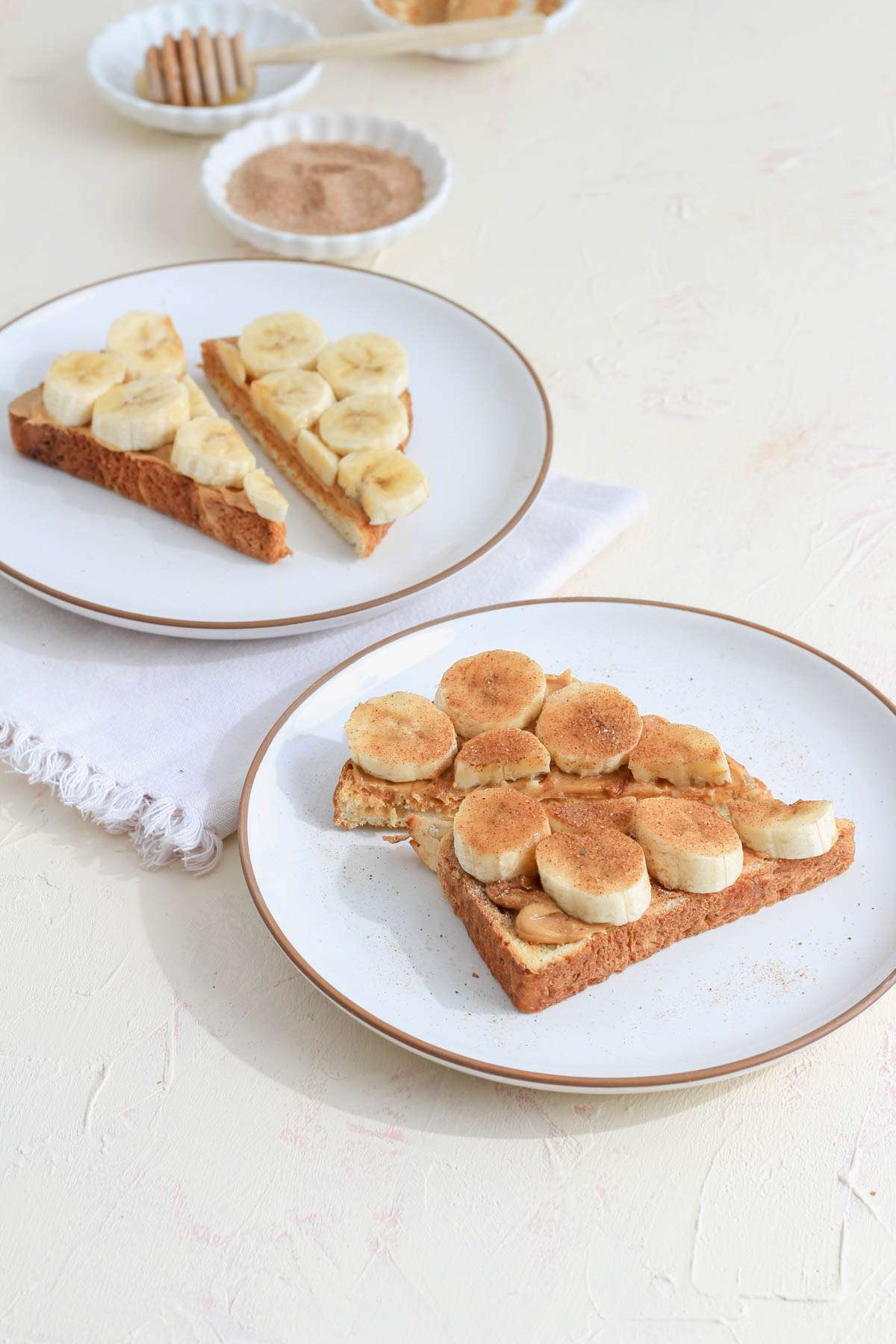 Peanut butter and banana on two slices of toast one with cinnamon sugar and one with honey.