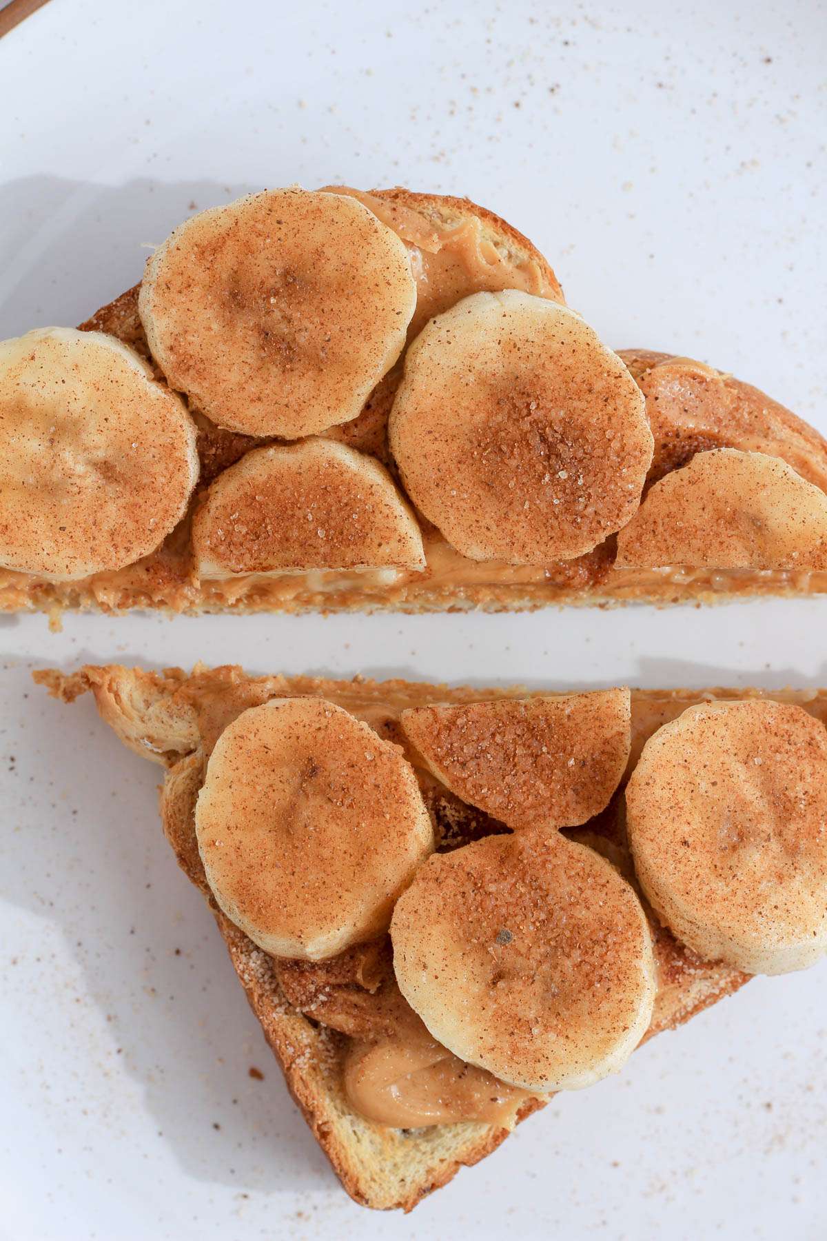 A top down picture of peanut butter banana toast with cinnamon sugar on a white plate.