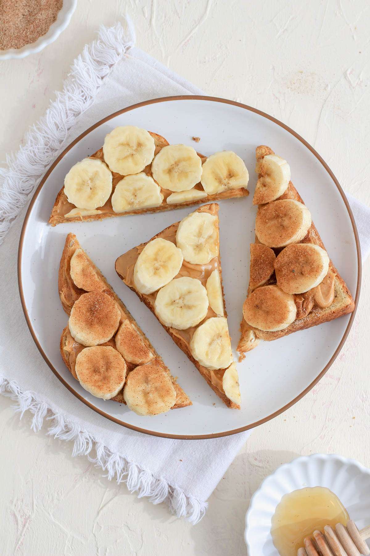 A white counter with a white towel topped with a white plate with four slices of peanut butter banana bread.