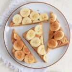 A white plate topped with four triangular slices of peanut butter banana toast.