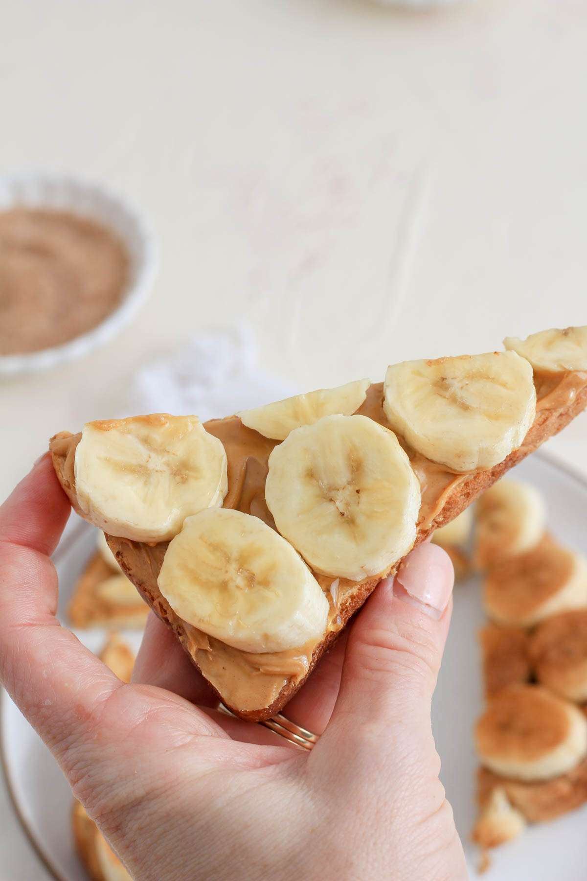 A hand holding a triangular slice of peanut butter banana toast.