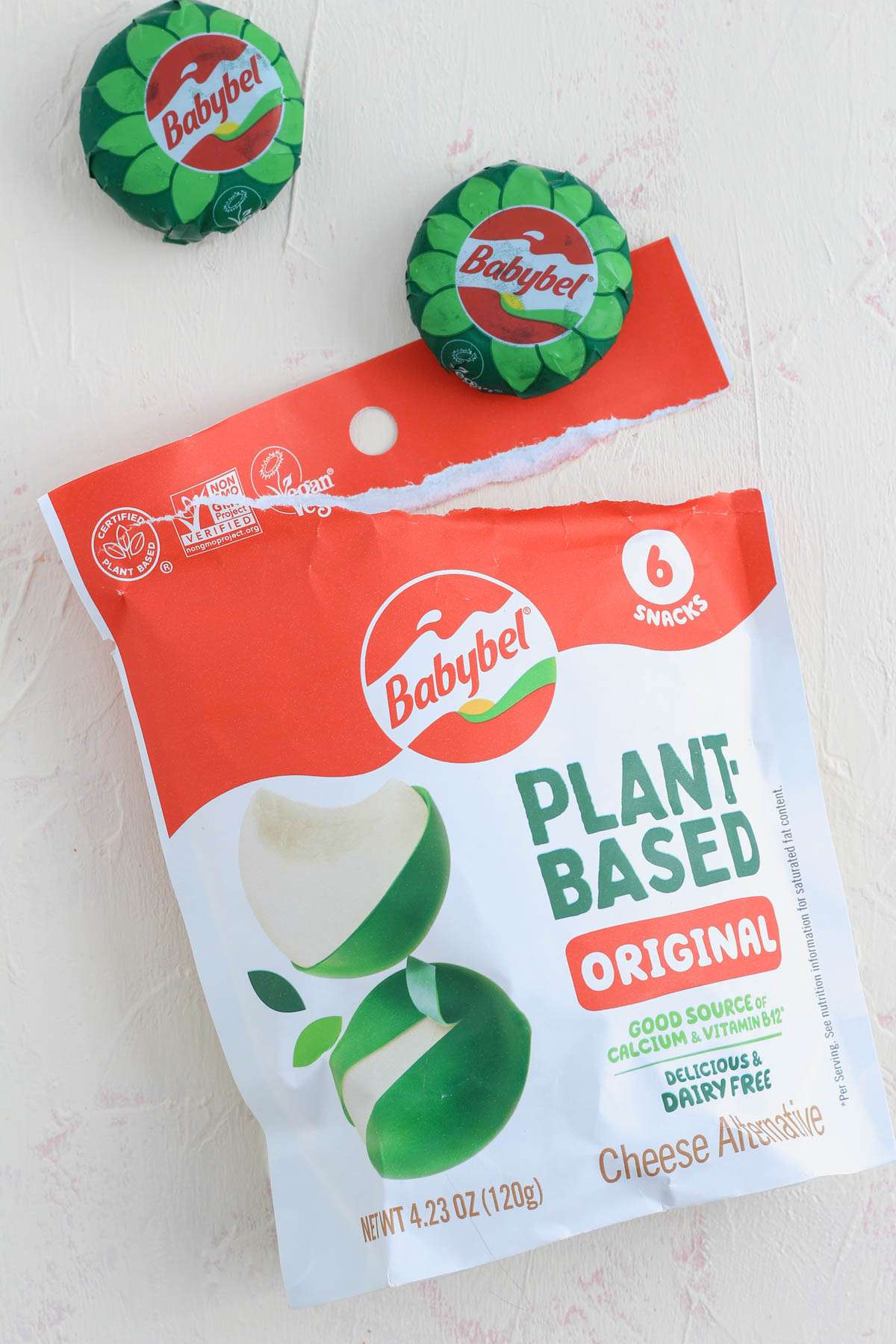 An open package of Original plant-based babybel cheese with two of the green cheese wheels on the counter.