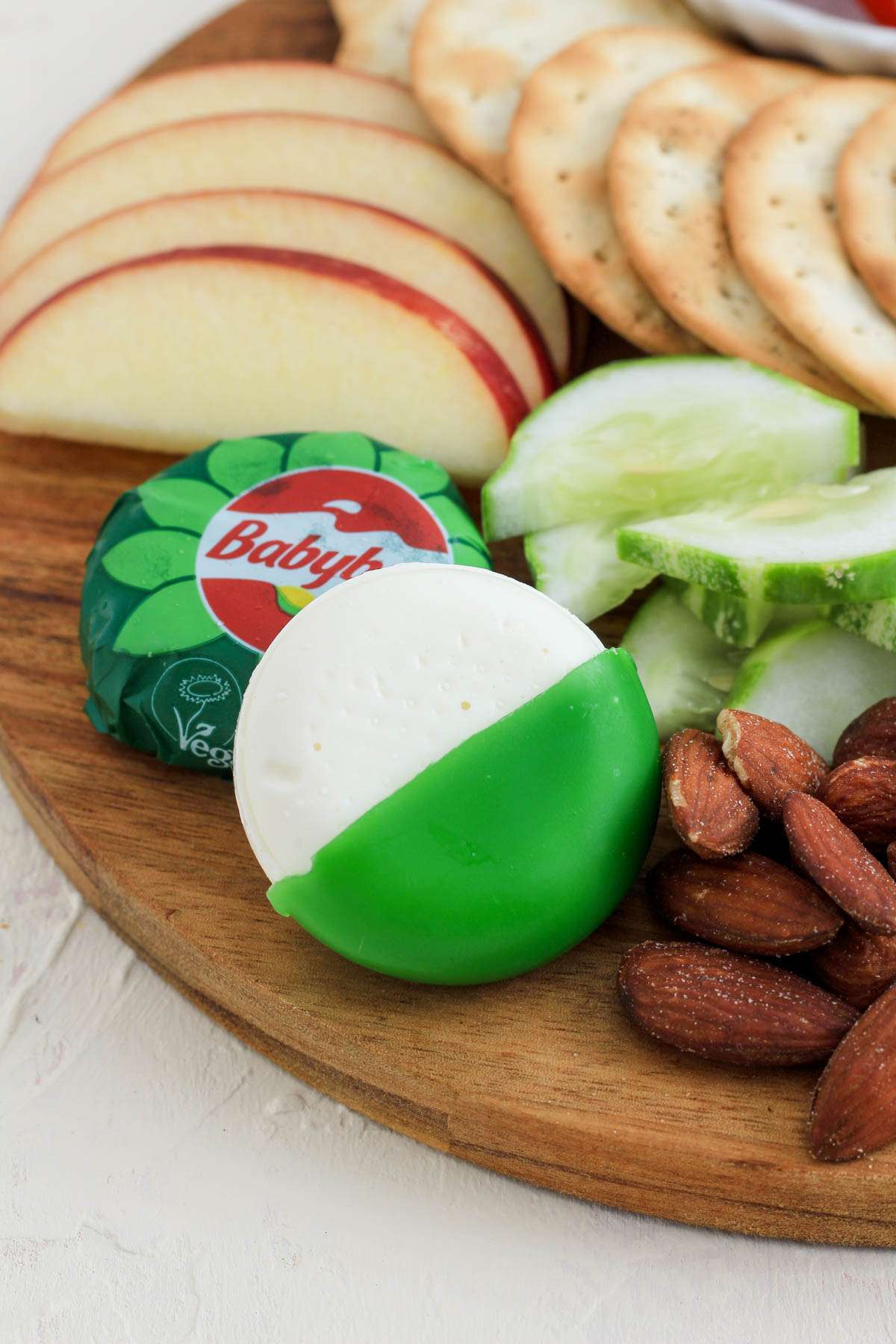 Vegan babybel cheese in a green wax wrapper on a wooden cutting board.