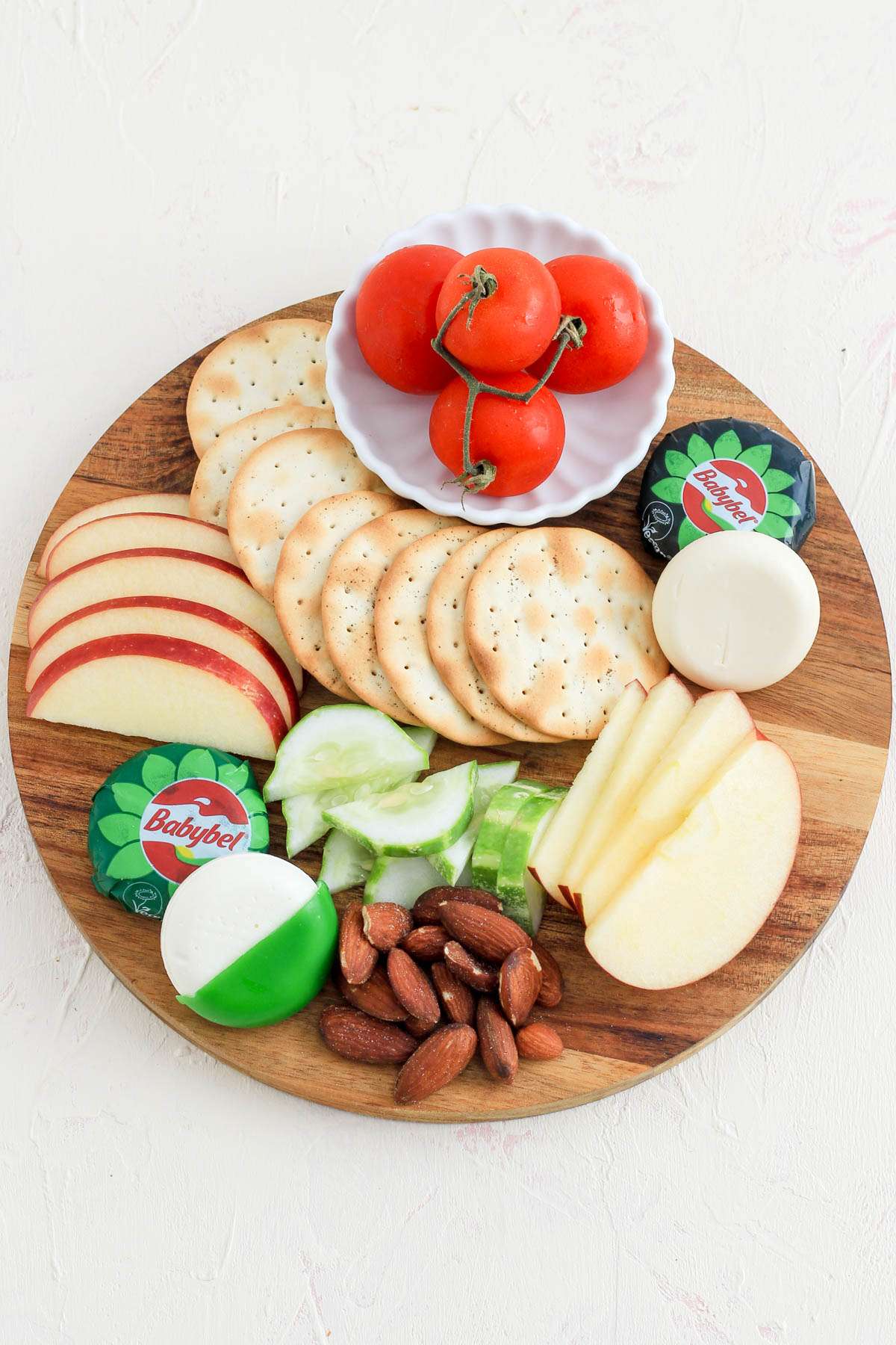 A top down image of a cheese board with mini plant-based babybel cheese wheels next to apples, crackers, cucumbers, and more!
