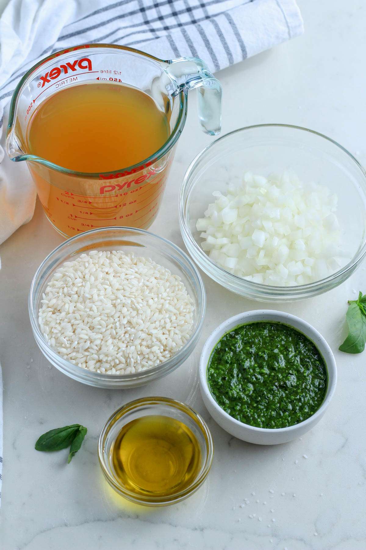 Ingredients for vegan pesto risotto on a white counter.