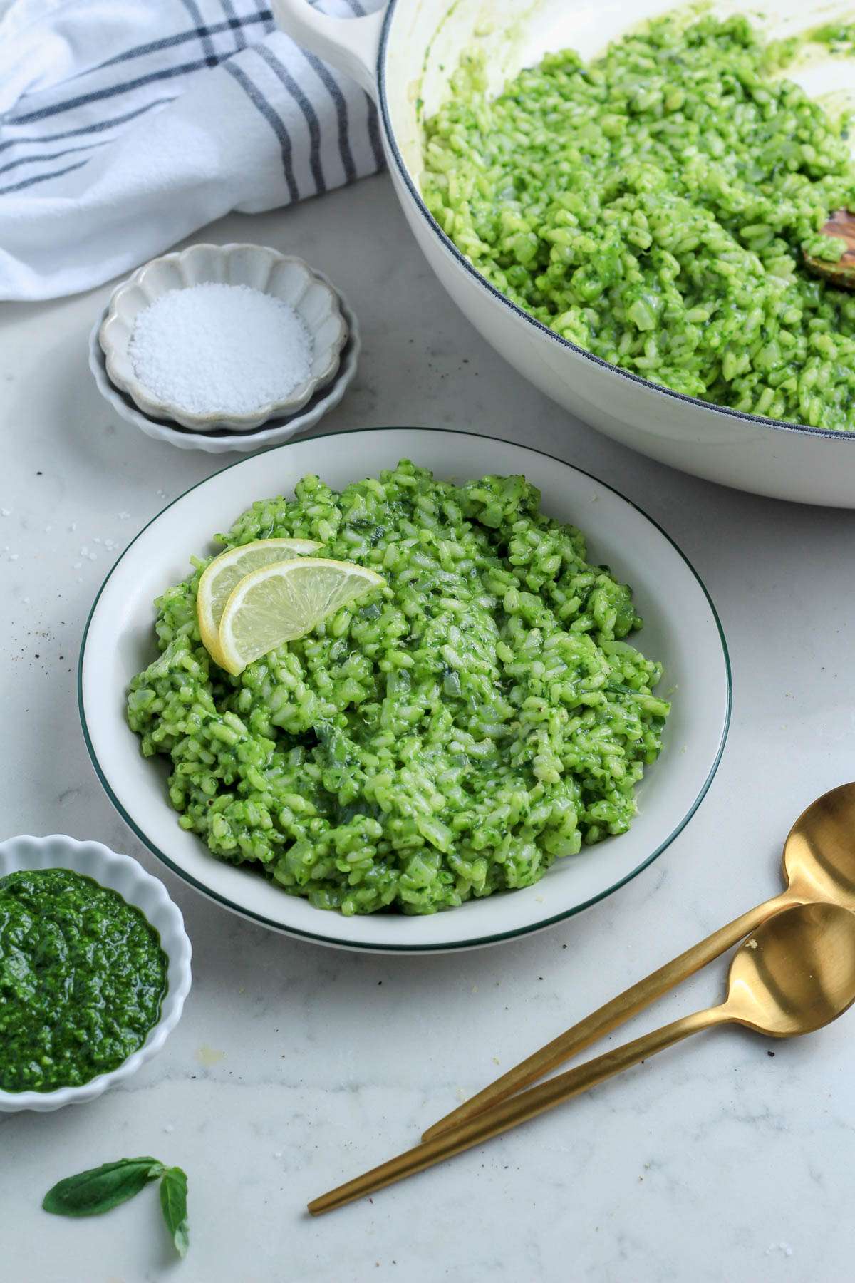 A bowl of vegan pesto risotto on a counter next to a small bowl of pesto and another bowl of salt.