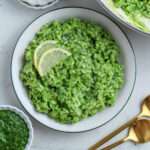 A small bowl of pesto risotto topped with some lemon slices on a white and green rimmed plate.